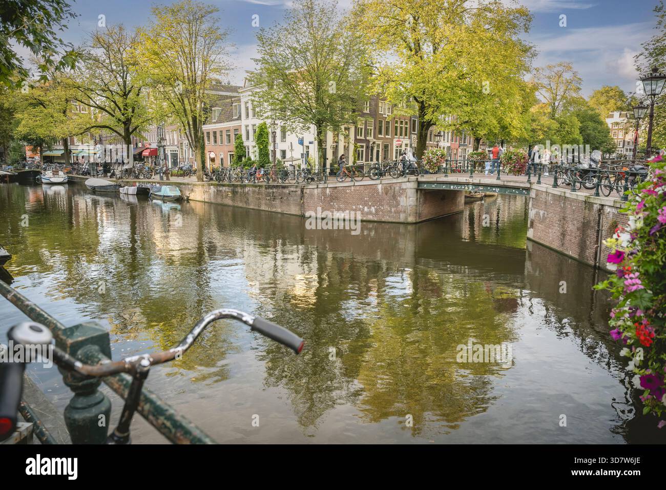 Vue panoramique sur le canal avec pont, vélos, bâtiments et arbres luxuriants sous un ciel bleu. Amsterdam,. Pays-Bas Banque D'Images
