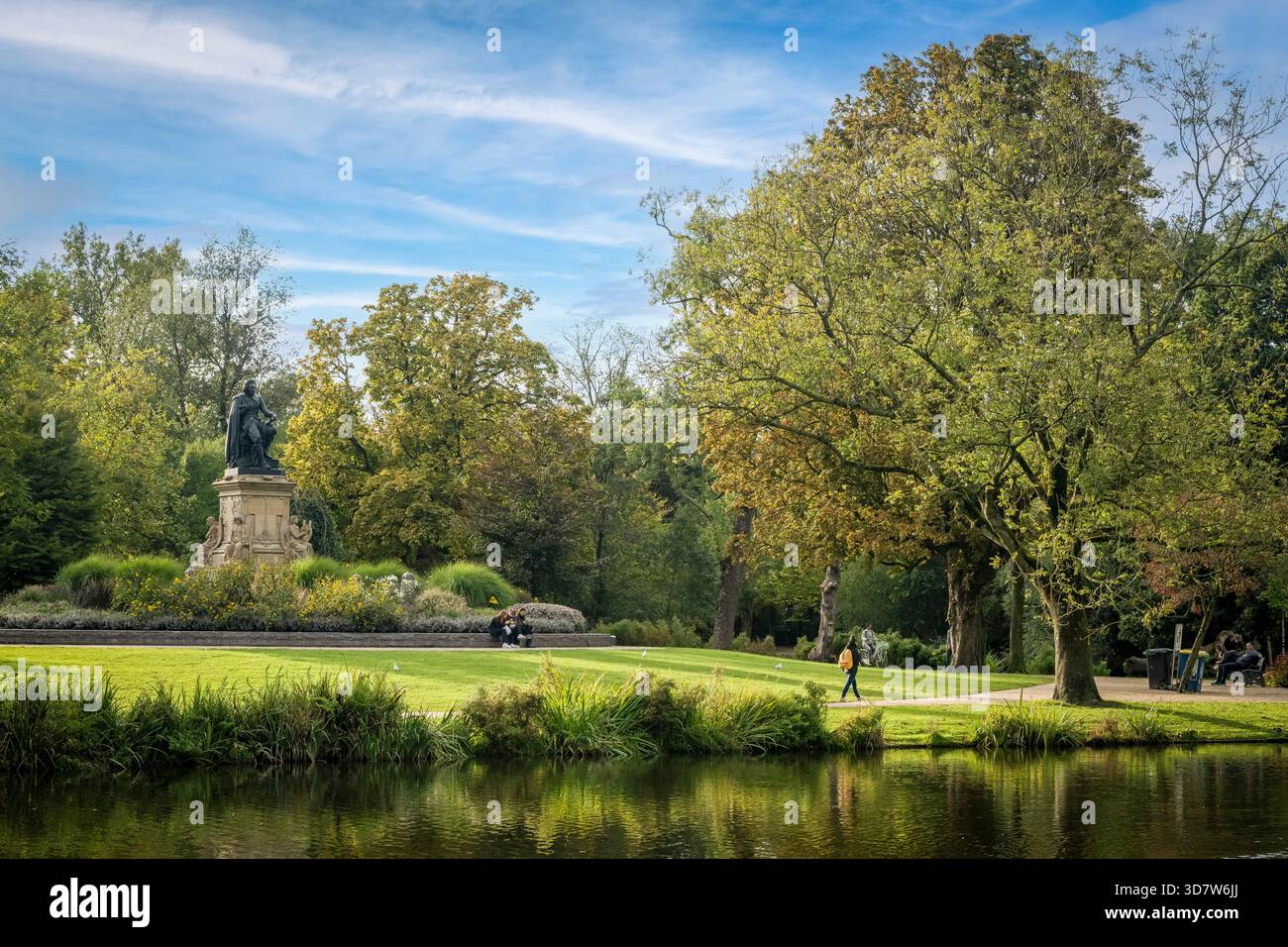 Un paysage de parc serein avec une statue, des sentiers pédestres et un étang réfléchissant sous un ciel bleu. Amsterdam,. Pays-Bas Banque D'Images