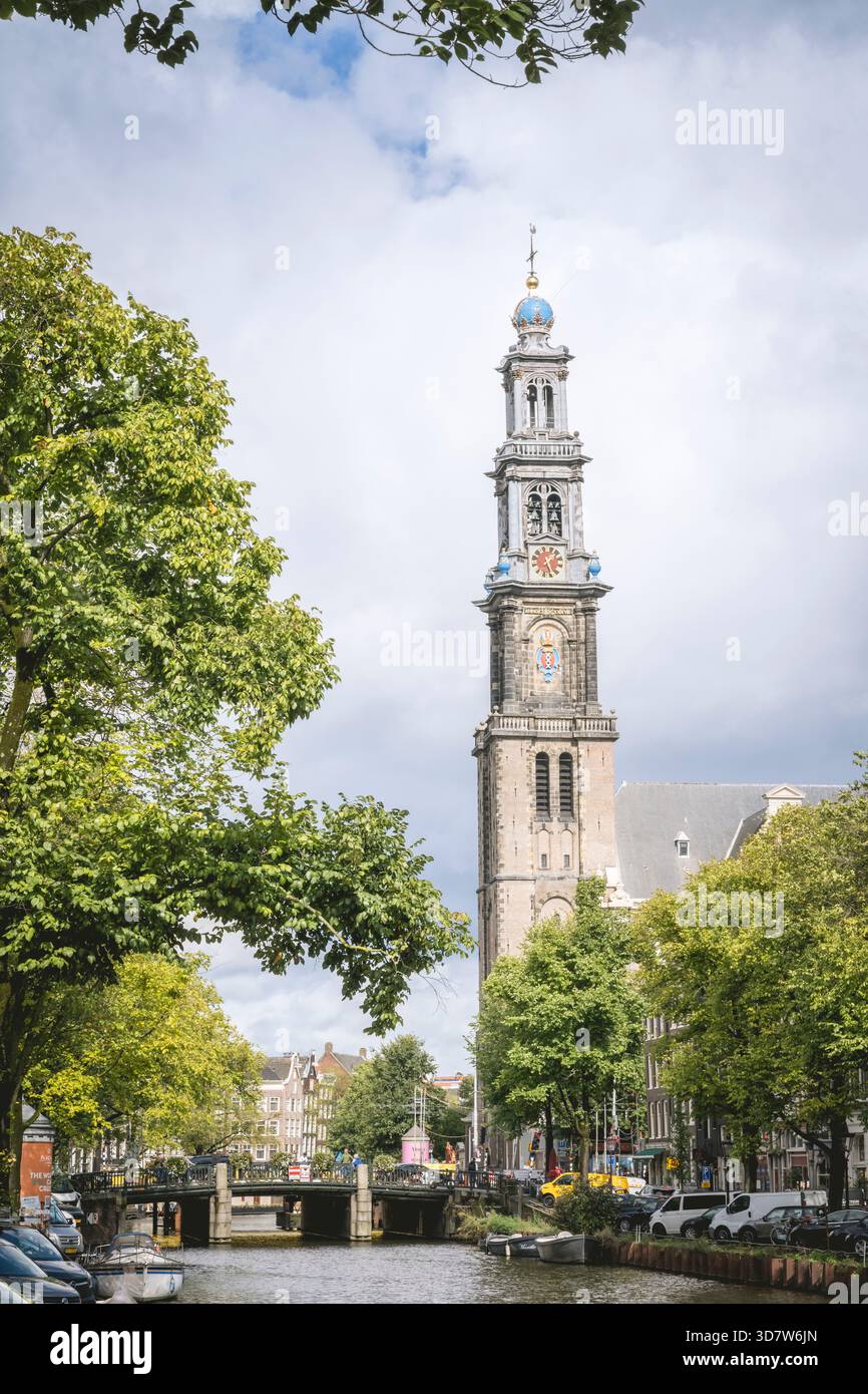 Haute tour de l'horloge dans une ville européenne avec des arbres et un canal sous un ciel nuageux. Amsterdam,. Pays-Bas Banque D'Images