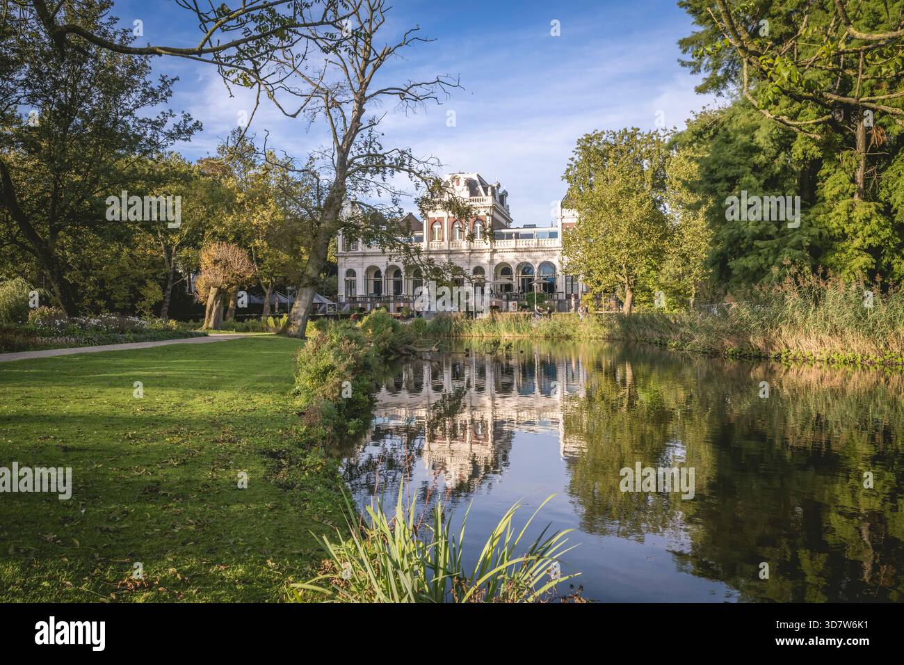 Grand bâtiment blanc entouré de verdure luxuriante et d'un étang réfléchissant sous un ciel bleu. Amsterdam,. Pays-Bas Banque D'Images