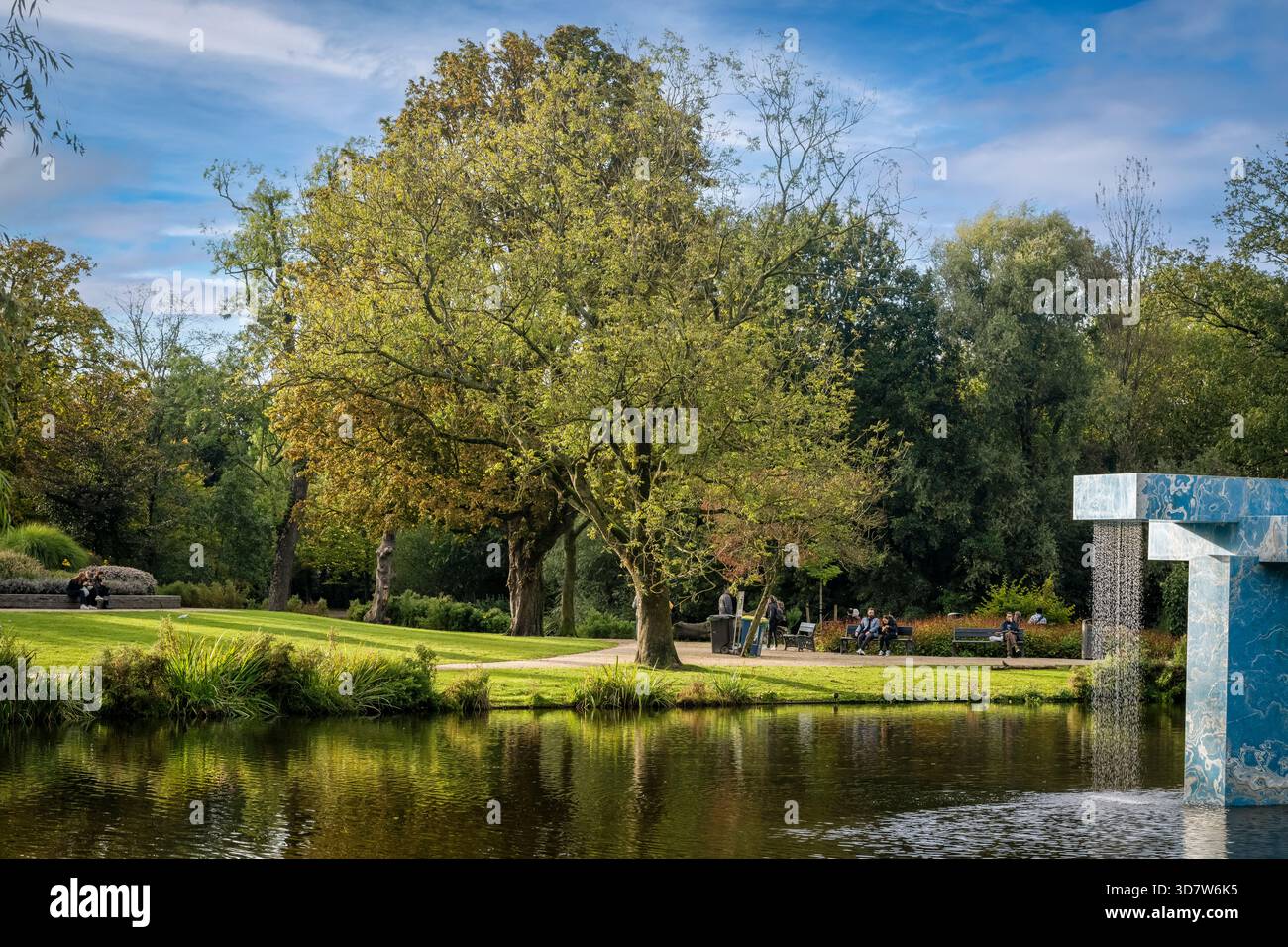 Scène de parc luxuriant avec un étang, des arbres, un chemin et une fontaine carrelée bleue. Amsterdam,. Pays-Bas Banque D'Images