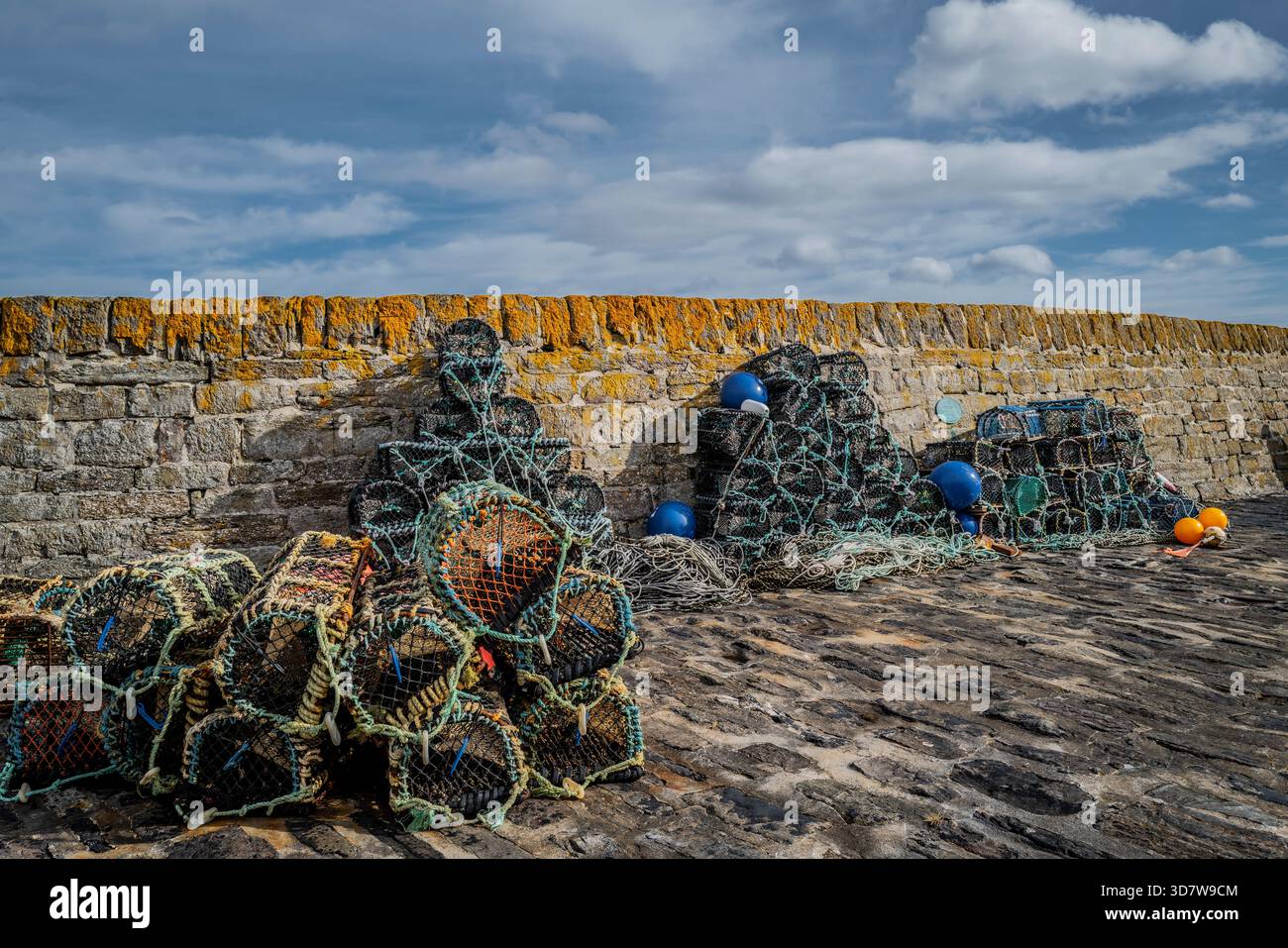Des piles de pots de homard et des bouées colorées sur un trottoir de pierre contre un mur de pierre altérée. Port de Keiss, Écosse Banque D'Images