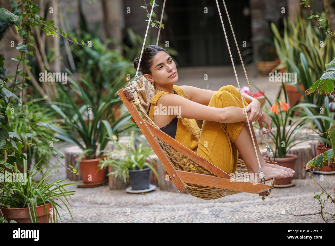 Femme en tenue jaune assise sur une balançoire entourée de plantes vertes luxuriantes. Sierra Alhamilla, Almeria, Espagne Banque D'Images