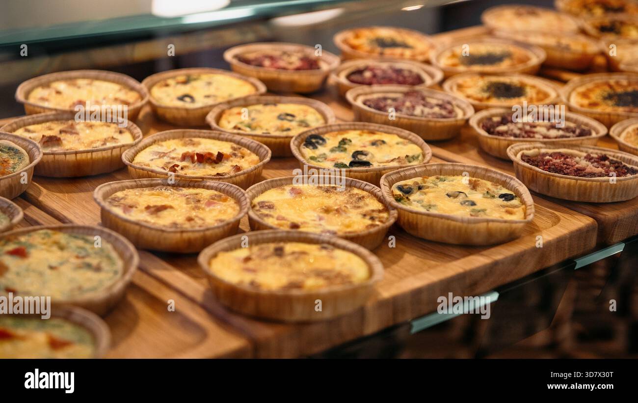 Gros plan de nombreuses mini-tartes et quiches fraîchement préparées sur un panneau d'affichage en bois. Nombreuses tartes aux garnitures salées (fromage, olives) Banque D'Images