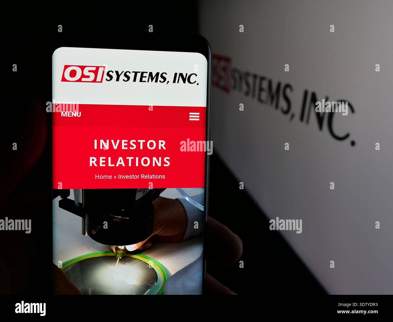 Stuttgart, Allemagne - 11-18-2025 : personne tenant un smartphone avec la page web de la société de sécurité américaine OSI Systems Inc sur l'écran devant le logo. Banque D'Images