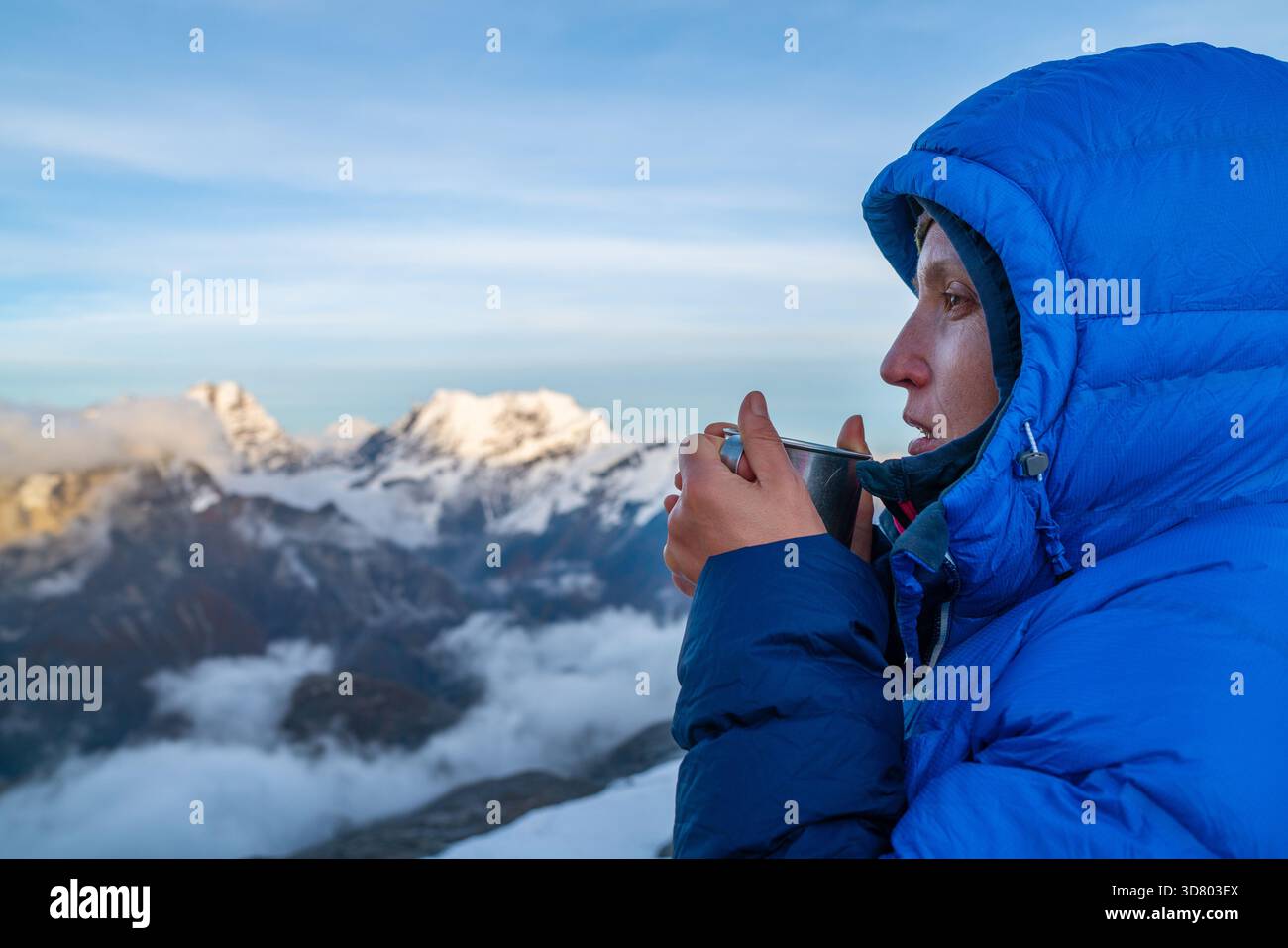Alpiniste de haute altitude habillée d'une veste rouge chaude de l'aube tenant une tasse en métal de thé chaud et boire une boisson chaude avec panorama de montagne Kangchenjunga Banque D'Images