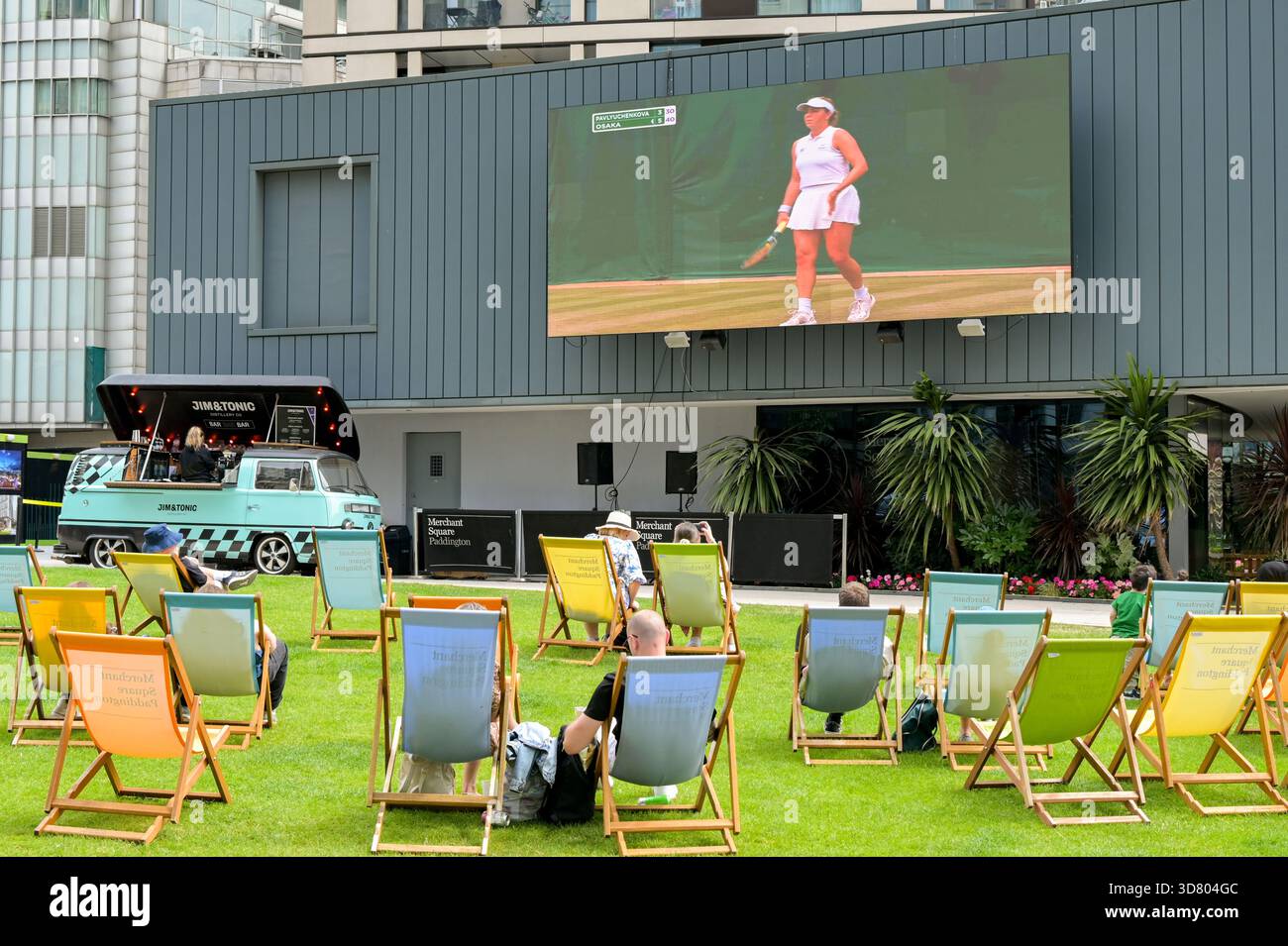 Londres, Angleterre, Royaume-Uni - 4 juillet 2025 : fans de tennis assis sur des transats sur une pelouse à Paddington regardant le tennis à Wimbledon sur un grand écran. Banque D'Images