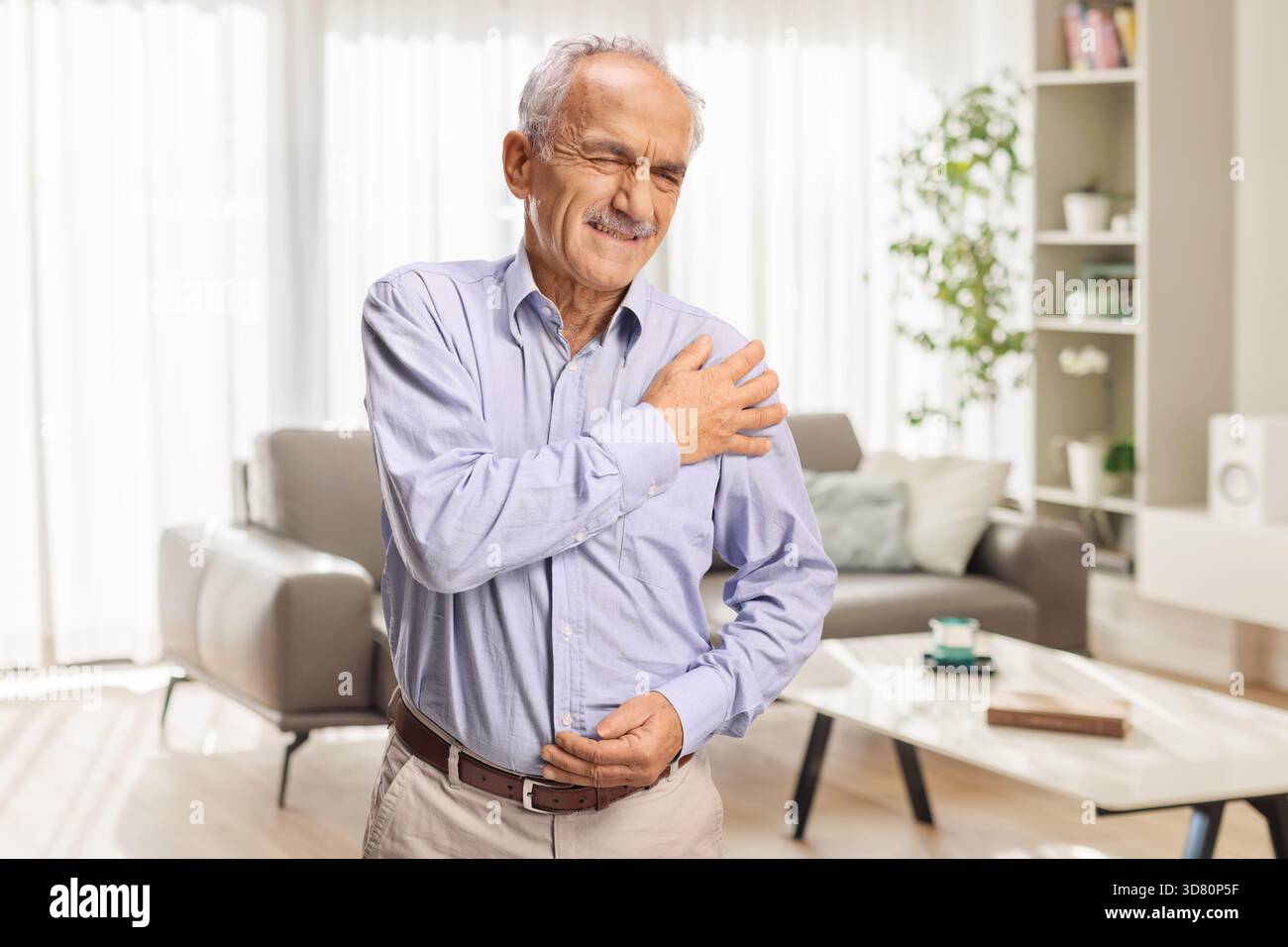 Homme âgé à la maison ressentant une douleur à l'épaule Banque D'Images