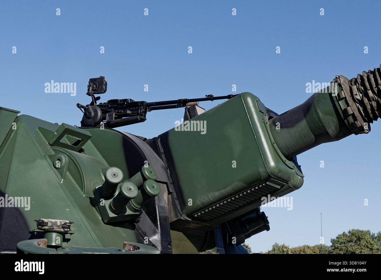 Gros plan du canon d'un obusier moderne et d'une mitrailleuse montés sur un véhicule militaire, contre un ciel bleu clair. Banque D'Images
