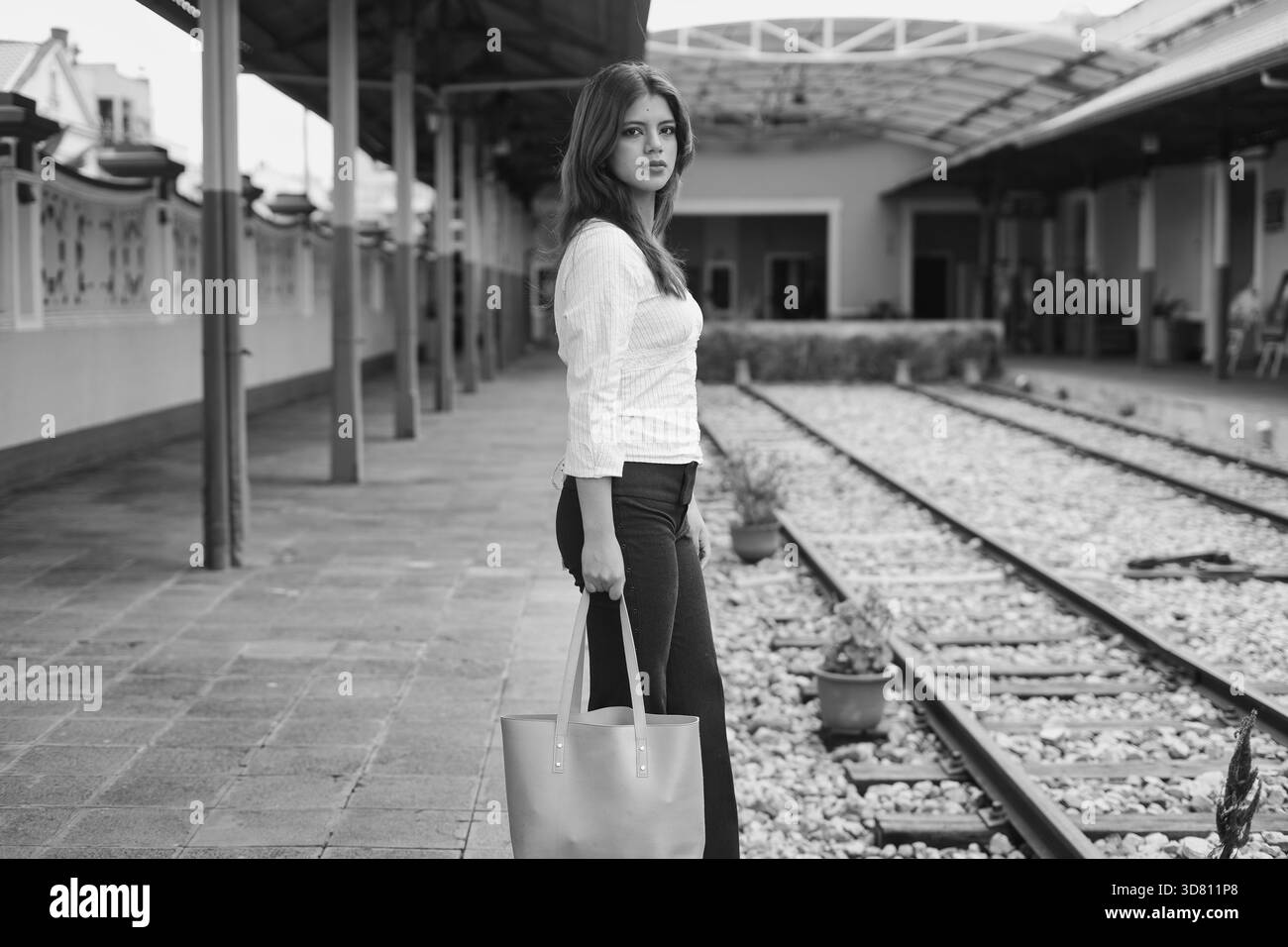 Jeune femme à la mode urbaine chemise blanche rayée, pantalon noir et tote stands sur une gare Banque D'Images