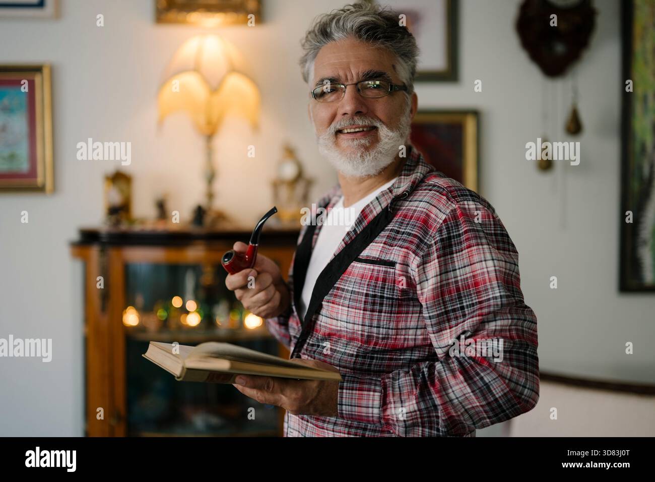 Homme senior profitant d'un moment calme avec un livre et une pipe Banque D'Images