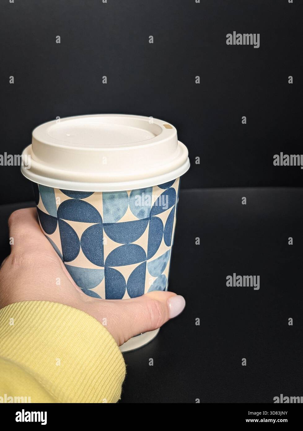 Gros plan d'une main tenant une tasse de café à emporter avec un motif géométrique sur un fond sombre Banque D'Images