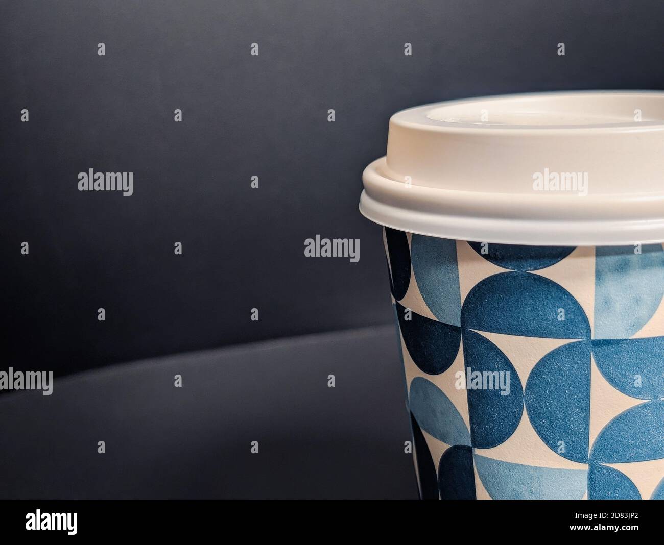 Gros plan macro extrême d'une tasse à café jetable avec motif géométrique bleu et couvercle blanc Banque D'Images