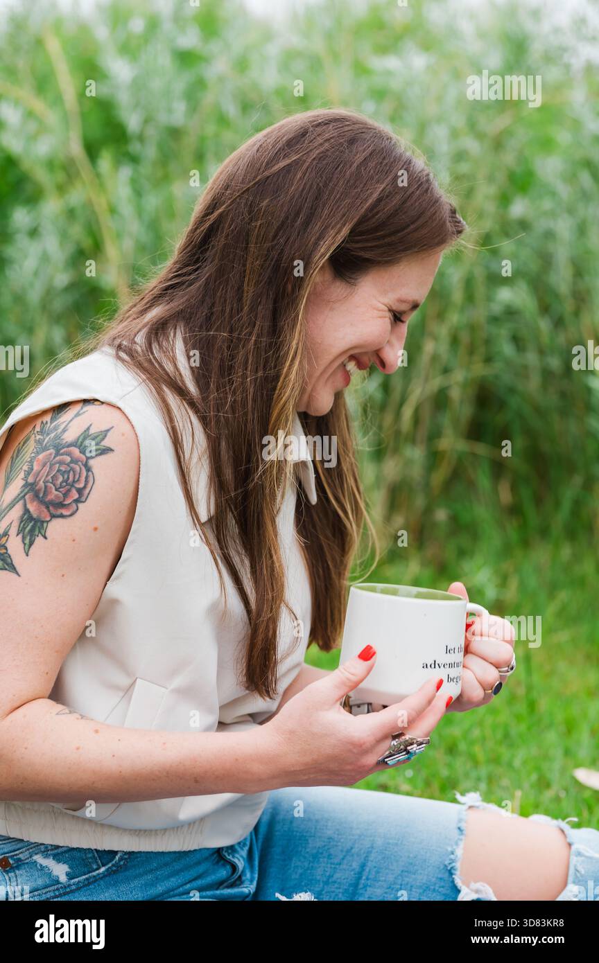 Femme riante tenant une tasse de café tout en étant assis sur l'herbe Banque D'Images