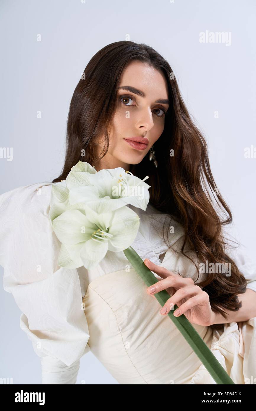 Une belle jeune mariée met en valeur son élégance et son charme, tenant un arrangement floral serein. Banque D'Images