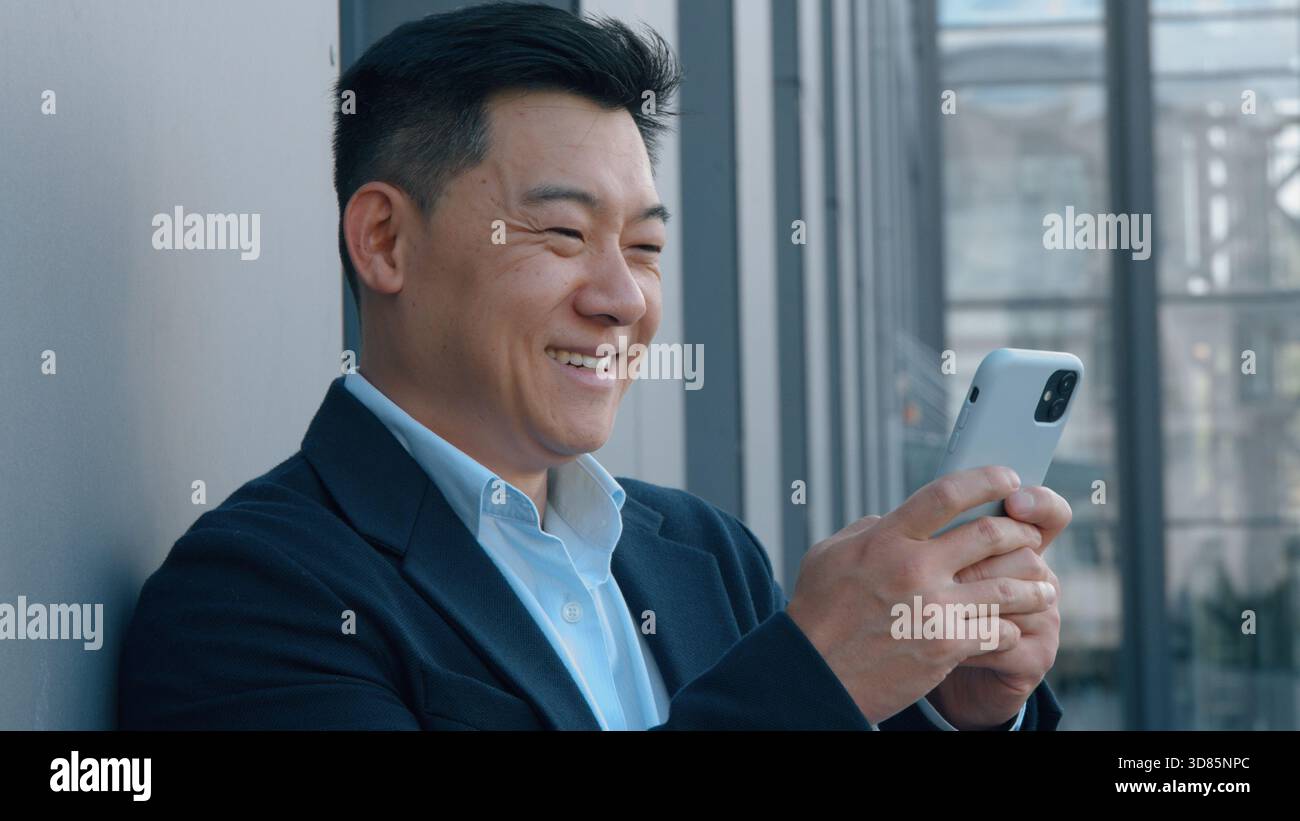 Souriant homme d'affaires asiatique d'âge moyen cherchant dans le téléphone travailleur coréen chinois homme d'affaires employeur japonais sourire positif utilisation sans soucis mobile Banque D'Images