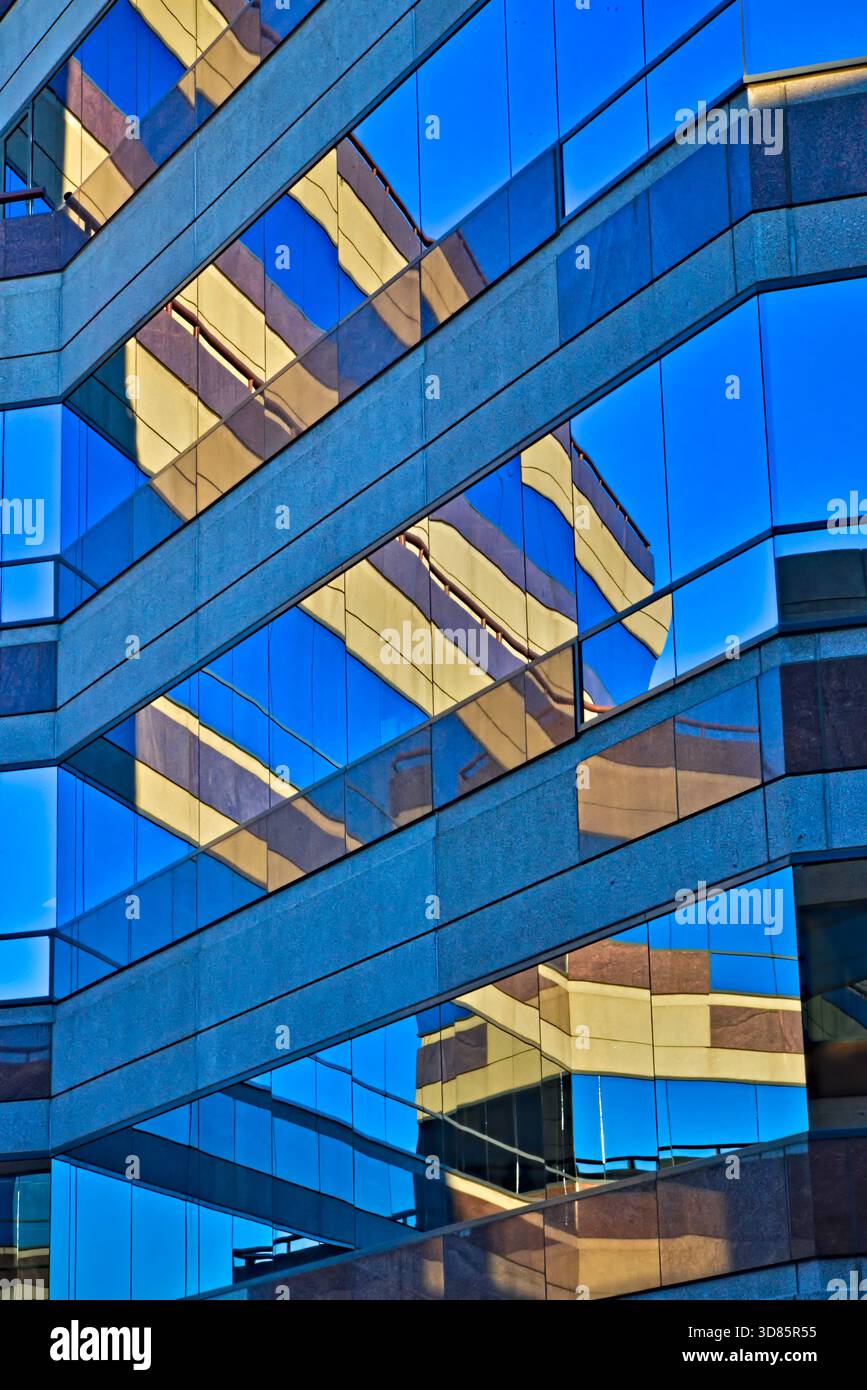 Façade géométrique en verre reflétant la structure d'un bâtiment adjacent, capturant un contraste de ciel bleu et de surfaces beiges. Banque D'Images