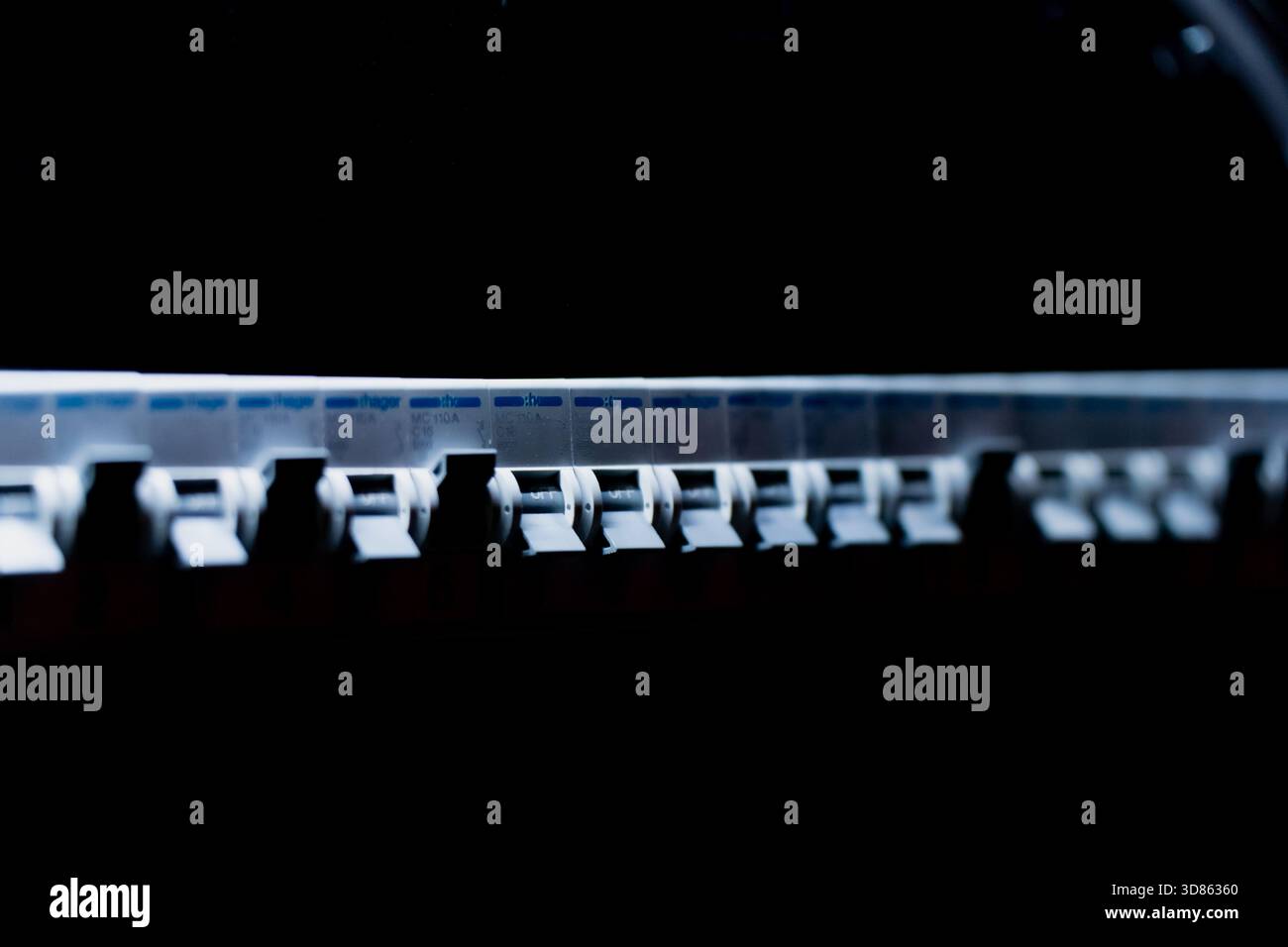 Rangée de disjoncteurs électriques alignés à l'intérieur d'un panneau d'équipement sombre, éclairé par un éclairage aérien focalisé qui met en évidence les commutateurs, étiquette Banque D'Images