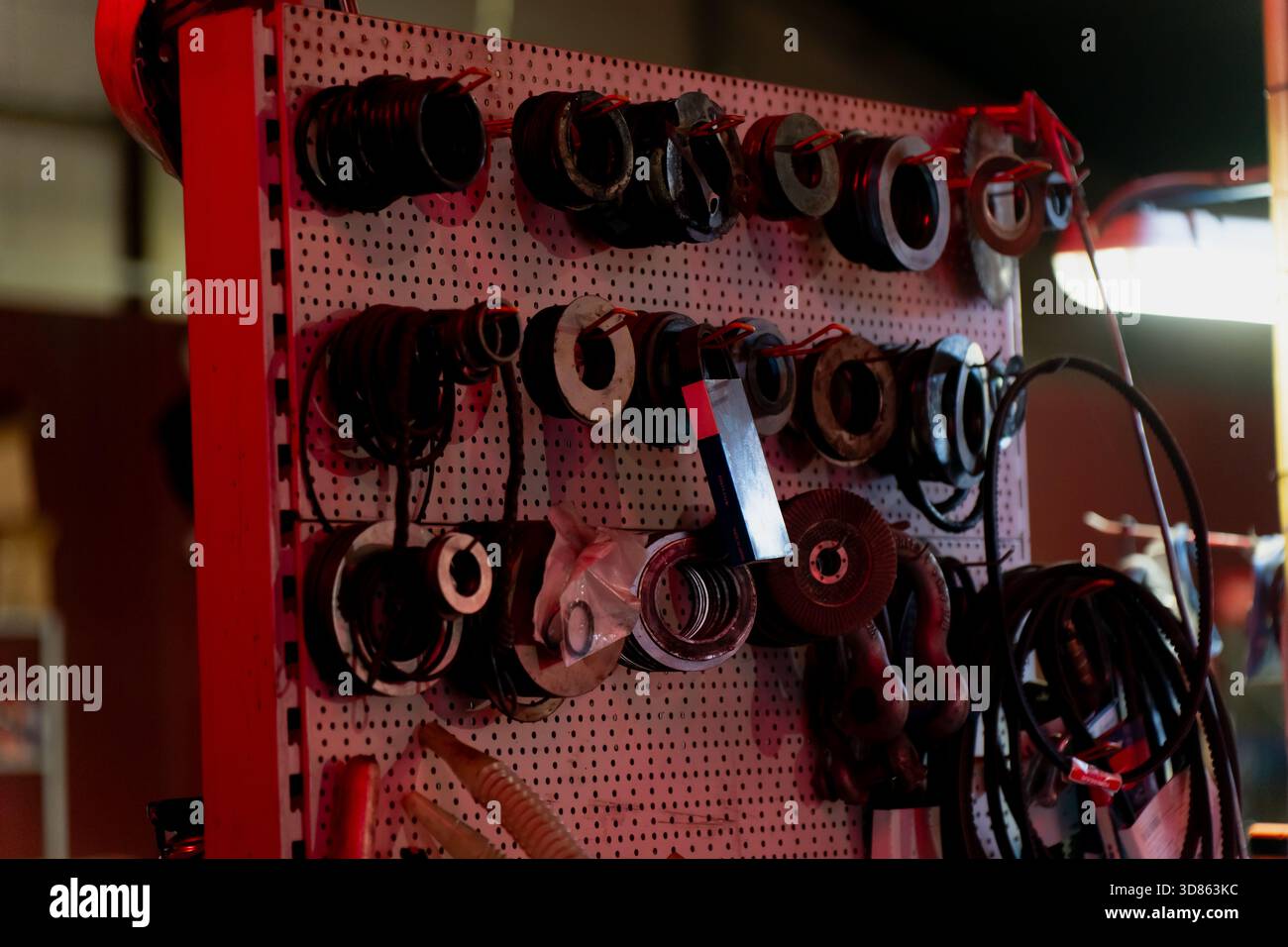 Surface de rangement organisée en panneaux perforés présentant plusieurs outils circulaires, rubans enroulés, câbles suspendus et divers articles d'atelier montés sur des crochets et h. Banque D'Images