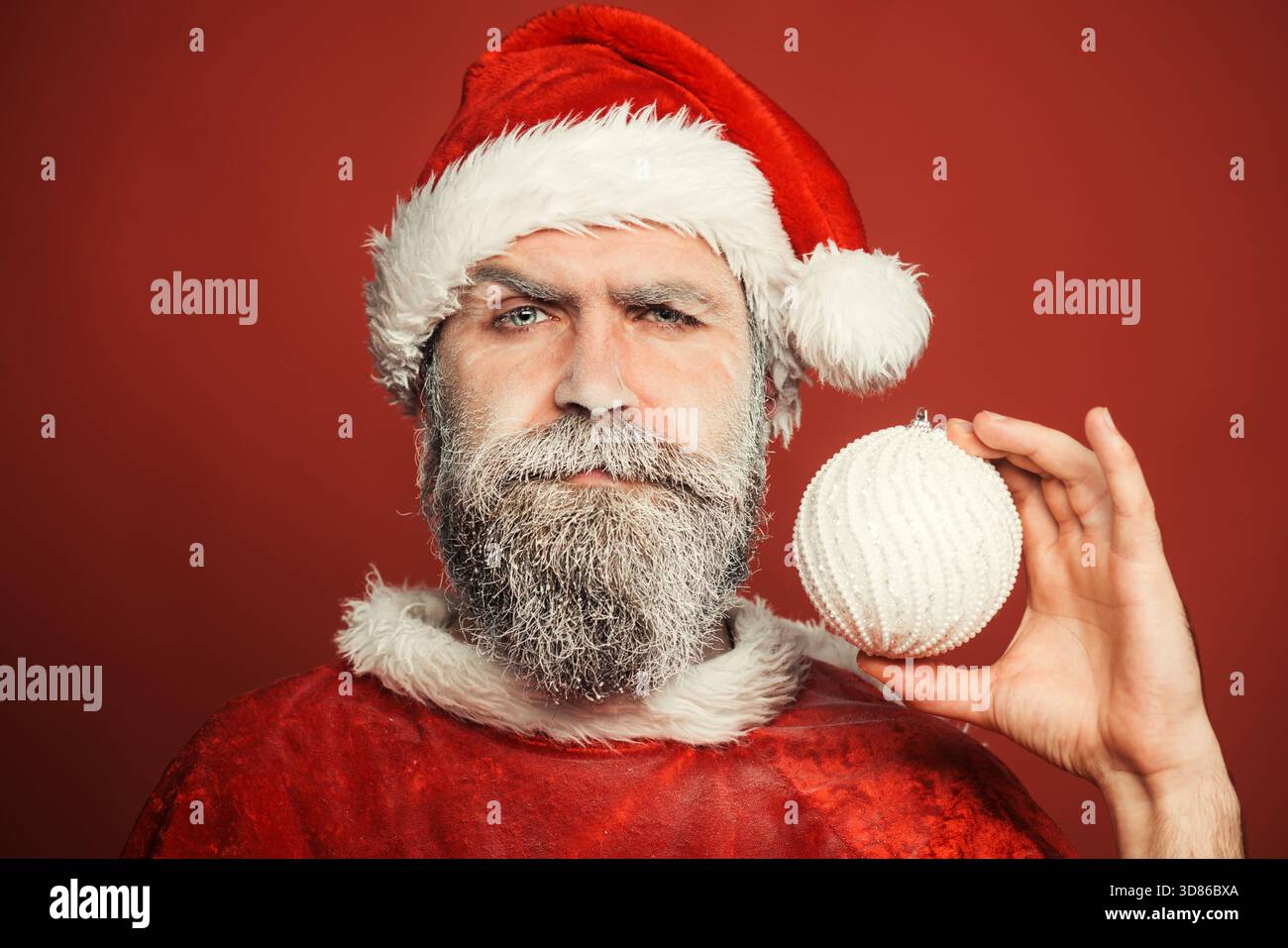 Joyeux Noël et bonne année. Le Père Noël avec barbe congelée tient une boule de Noël. Homme barbu dans le chapeau de Père Noël avec le jouet du nouvel an. Homme sérieux dans Banque D'Images