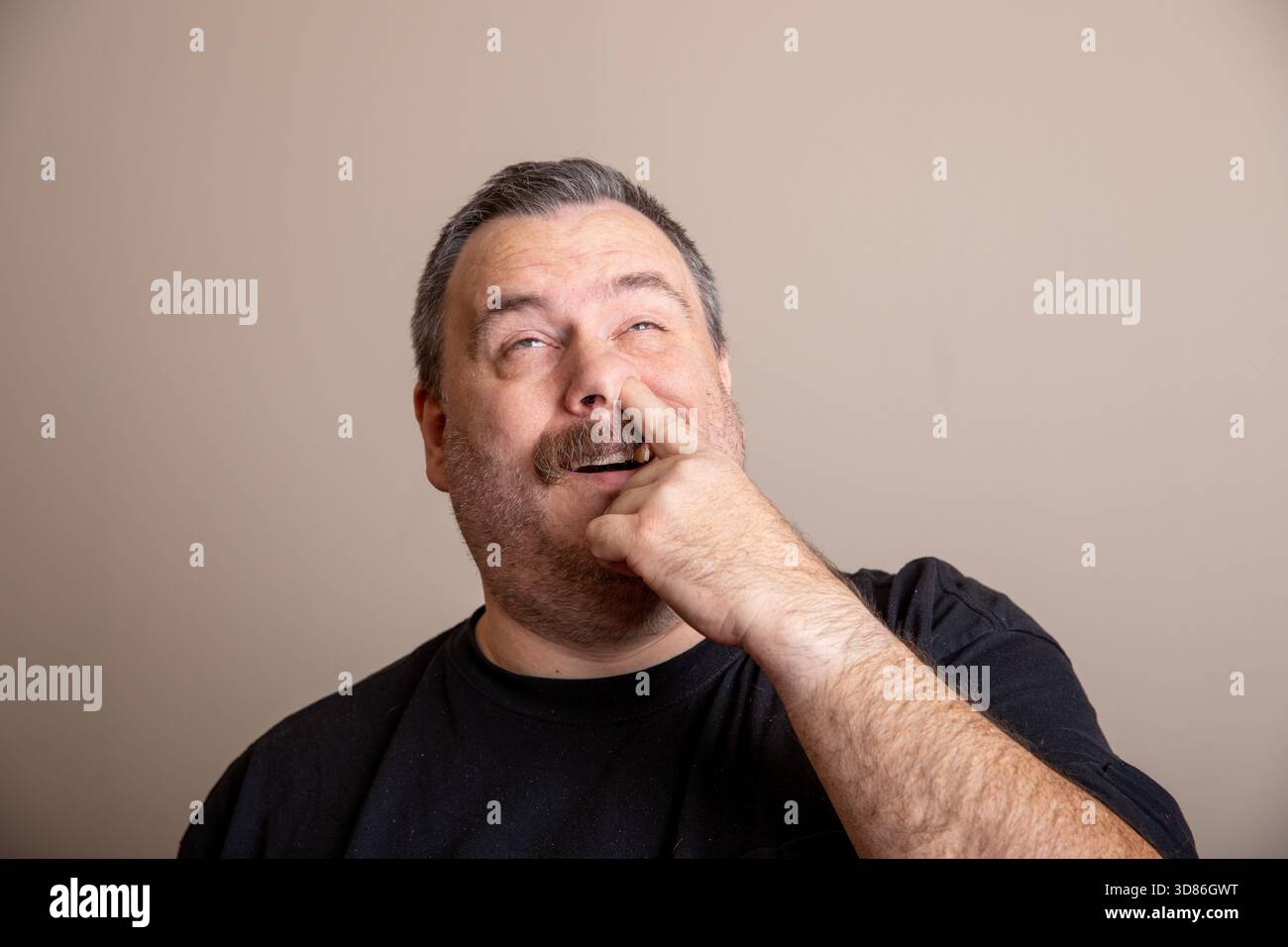 Un homme avec une barbe et une moustache fait un drôle de visage et pointe son doigt. Il porte une chemise noire et il est d'humeur ludique Banque D'Images
