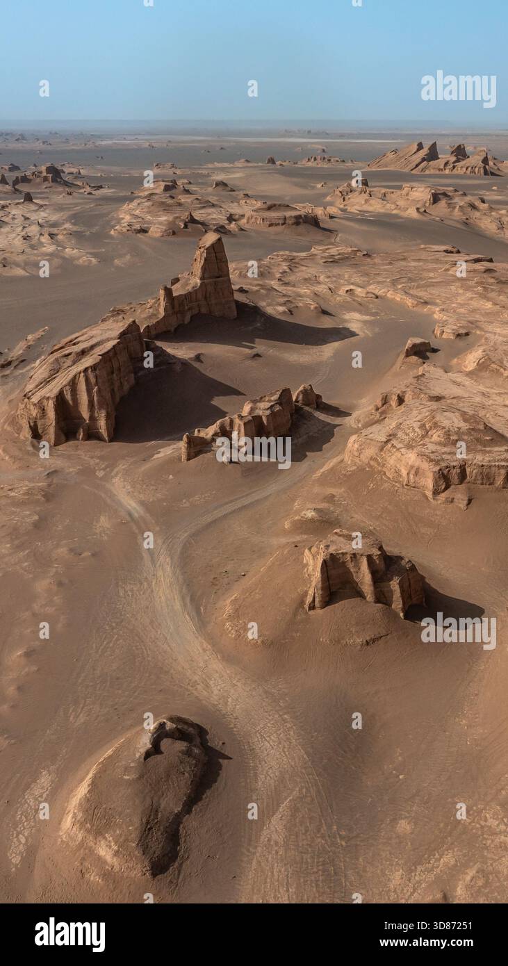 Vue aérienne des yardangs sculptés par le vent s'élèvent majestueusement du sol du désert chauffé par le soleil, projetant de longues ombres sous le ciel clair, Shahdad, Kerman Pro Banque D'Images