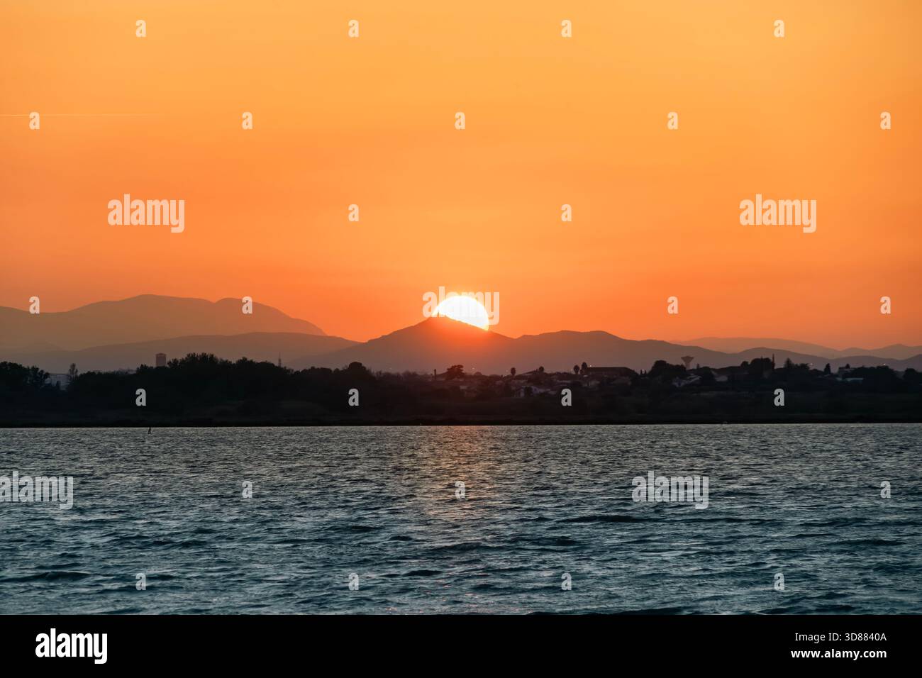 Le soleil se couche ou se lève derrière les collines côtières de Collioure, en France, projetant une lumière orange intense et silhouettant la ville historique Banque D'Images