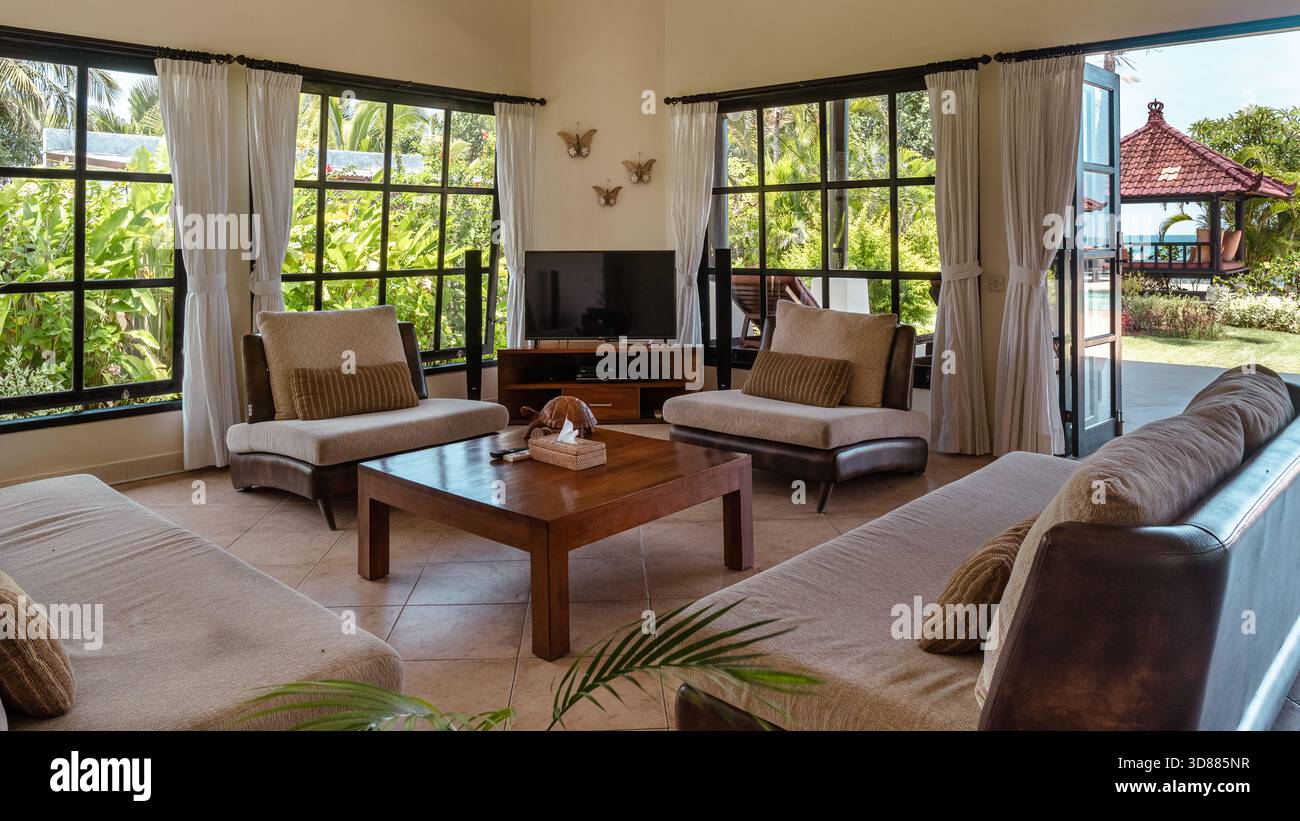 Un salon avec une grande fenêtre et une télévision. La chambre est remplie de meubles confortables, y compris des canapés et des chaises. Banque D'Images