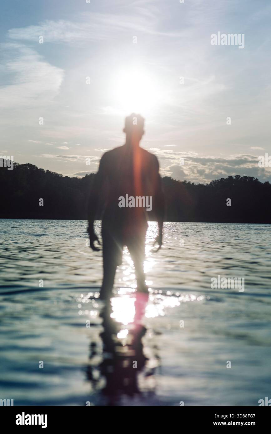 Scène tranquille de ciel ensoleillé avec l'homme debout dans l'eau du lac Banque D'Images