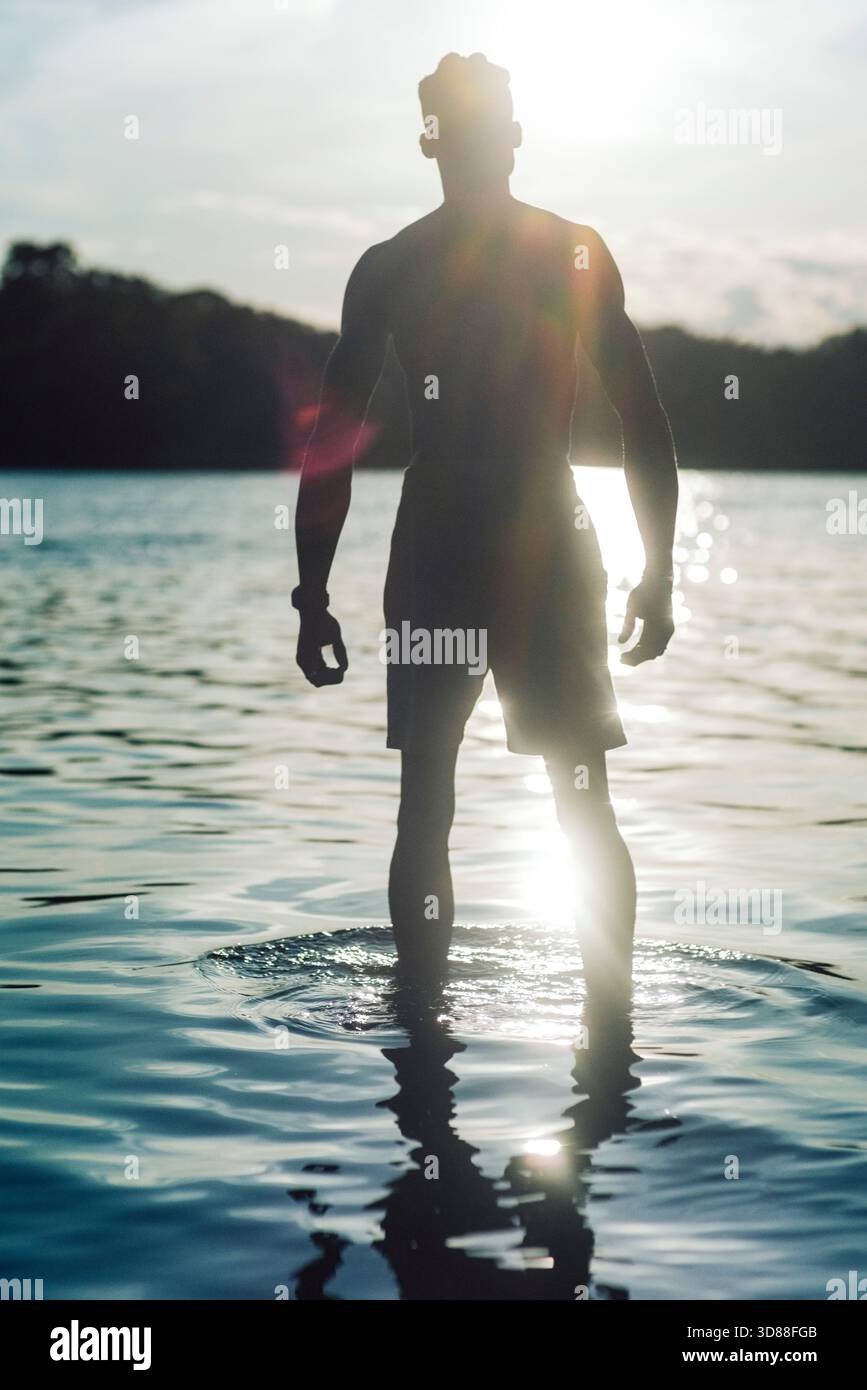 Lumière du soleil brillante sur la silhouette prise de vue de l'homme debout dans l'eau du lac Banque D'Images