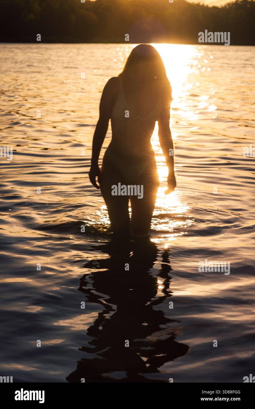Photo en silhouette d'une femme debout dans l'eau du lac à l'aube Banque D'Images