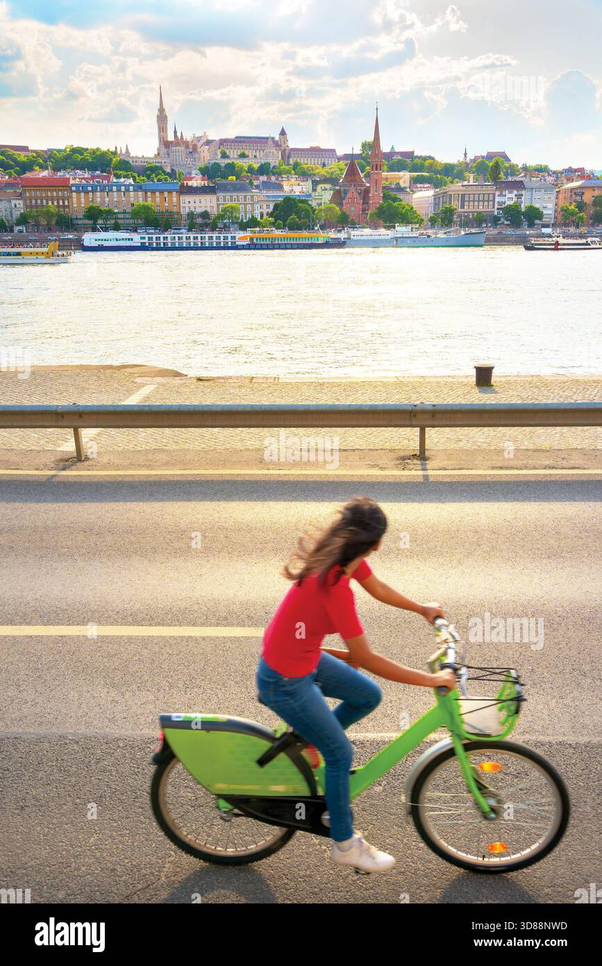 Fille chevauchant un vélo le long de la rive de la rivière contre la vieille vue de la ville Banque D'Images