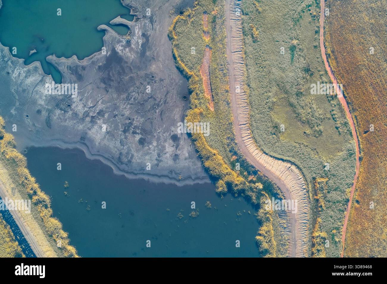 Vue de haut en bas par drone capturant la limite nette créée par un chemin de terre sinueux entre un lac contaminé sombre et un champ brun labouré. Gravité de la crise écologique et dommages environnementaux Banque D'Images