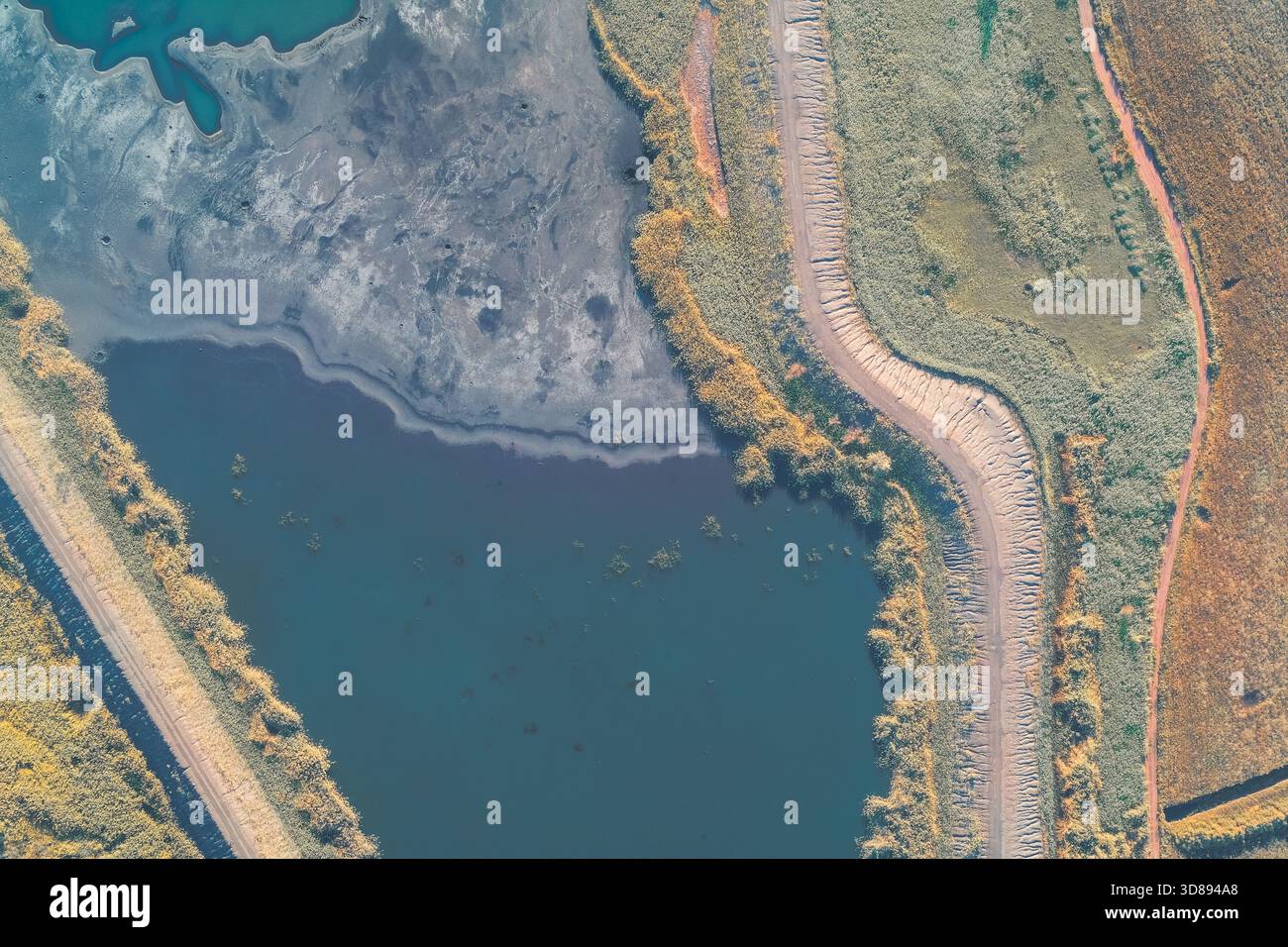 Vue de drone abstraite capturant la limite complexe à double voie séparant le lac industriel sombre et contaminé de la végétation luxuriante et d'un champ brun. Gravité de la crise écologique. Banque D'Images