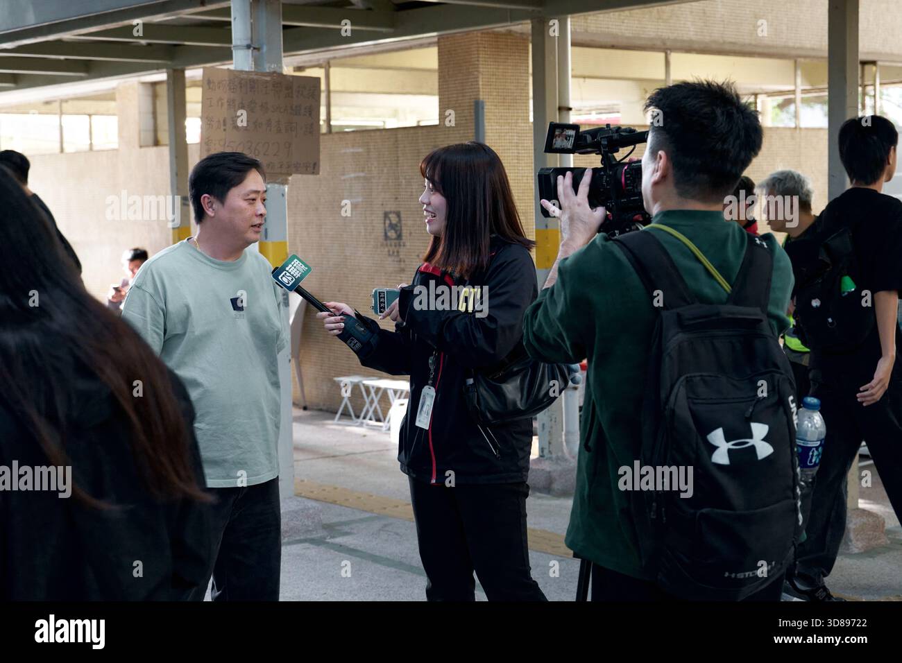 Un journaliste de CTS, une chaîne de télévision taïwanaise, mène une interview avec une locale devant un membre de son équipe de tournage à Tai po, Hong Kong. Banque D'Images