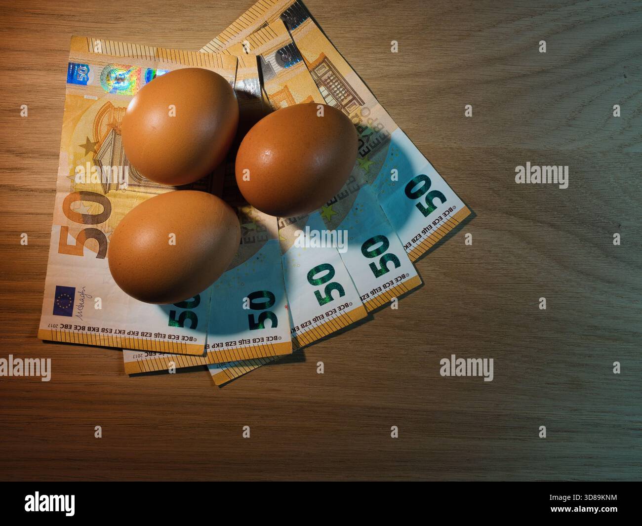 Inflation alimentaire : oeufs et monnaie en euros - trois oeufs bruns reposant sur des billets de 50 euros en éventail sur une table en bois. Symbolise la hausse des coûts alimentaires, l'inflation, Banque D'Images