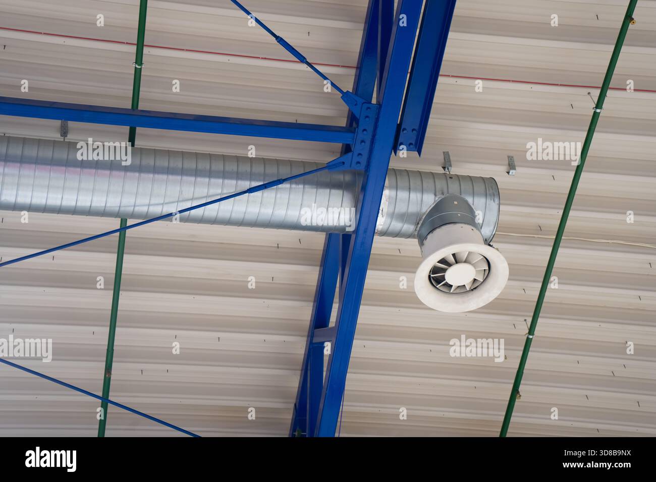 Conduits de ventilation exposés et sortie d'air montée au plafond installés sur des poutres de support en acier bleu, montrant l'infrastructure HVAC dans l'intérieur industriel Banque D'Images