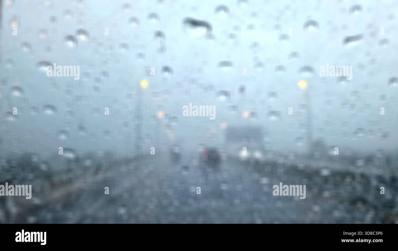 Image floue de gouttes de pluie sur le pare-brise d'une voiture un jour de pluie sur une autoroute. Banque D'Images