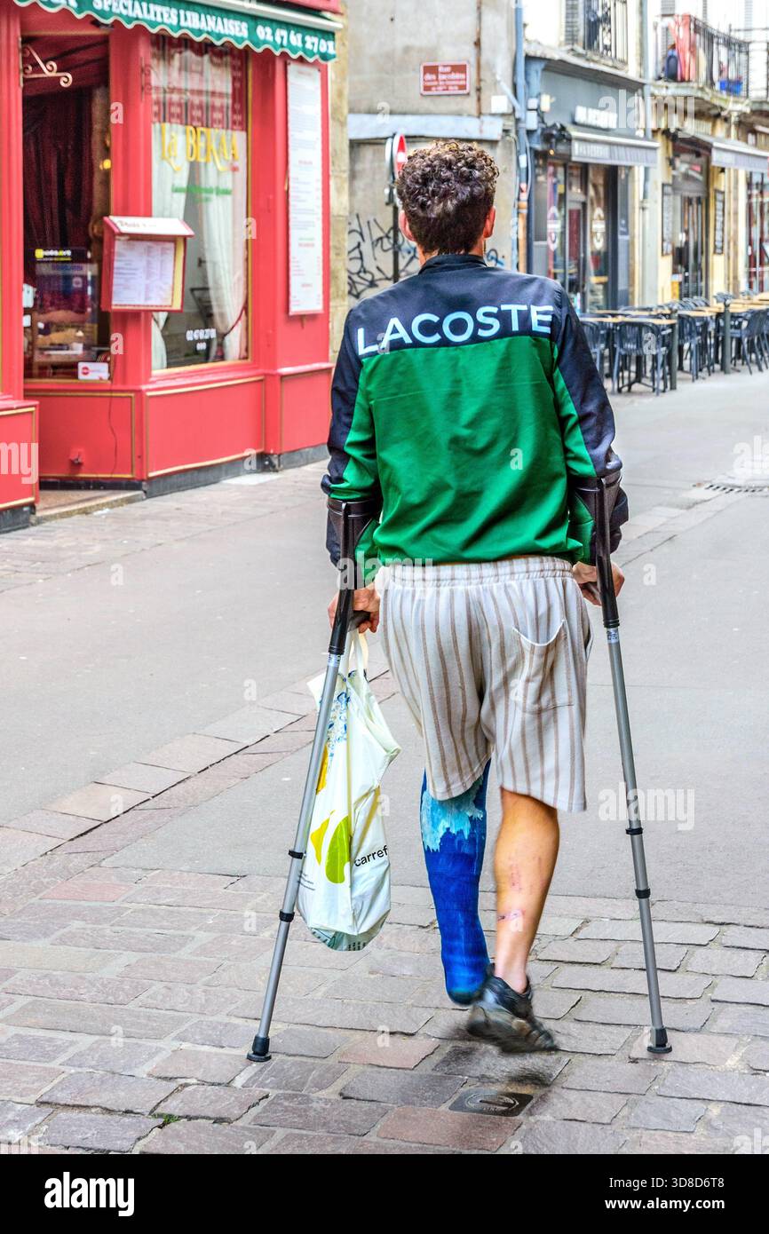Jeune homme avec jambe cassée en plâtre utilisant des béquilles médicales d'avant-bras comme aide à la marche dans le centre-ville - Tours, Indre-et-Loire (37), France. Banque D'Images
