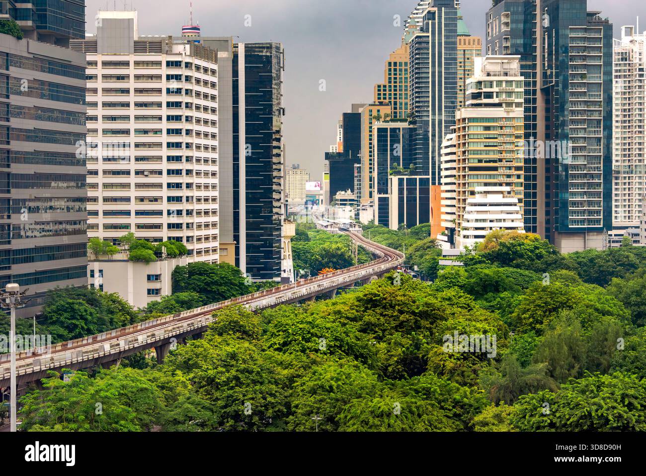 Une végétation luxuriante rencontre des gratte-ciels modernes dans un paysage urbain, avec une ligne de train surélevée coupant à travers les arbres, Bangkok, Thaïlande. Banque D'Images