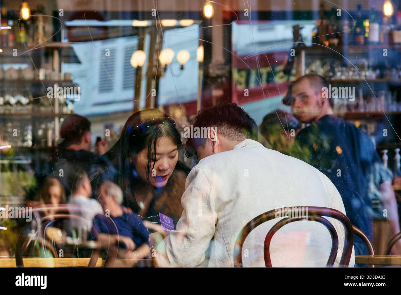 Paris, France - mai 2025 : à Montmartre, un couple s'engage dans une discussion animée au Bar le Progres. Leurs reflets se fondent dans l'atmosphère animée Banque D'Images