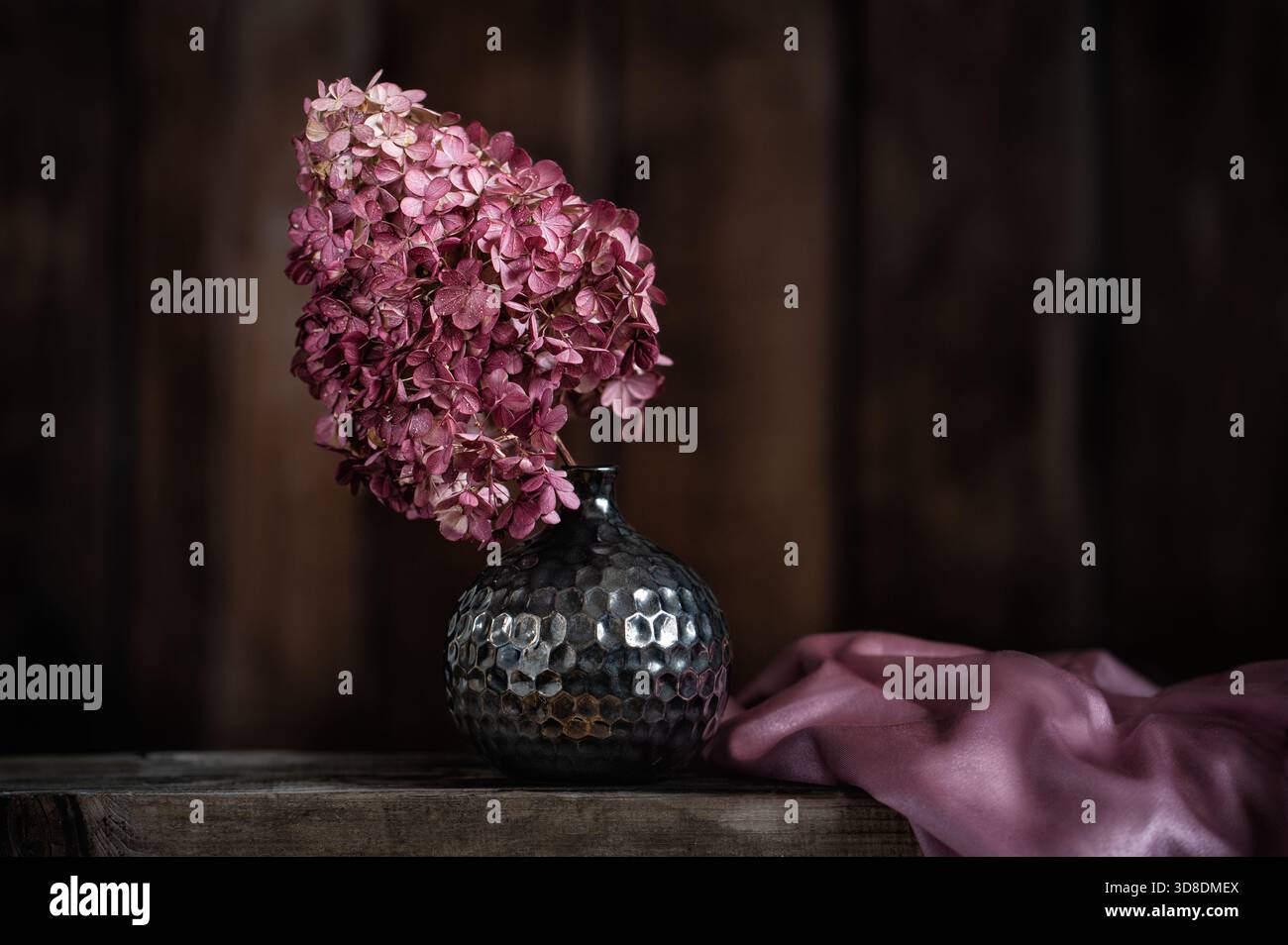 Composition de nature morte vintage avec des fleurs d'hortensia rose séchées dans un vase marron décoratif avec motif texturé sur une surface en bois rustique. Banque D'Images