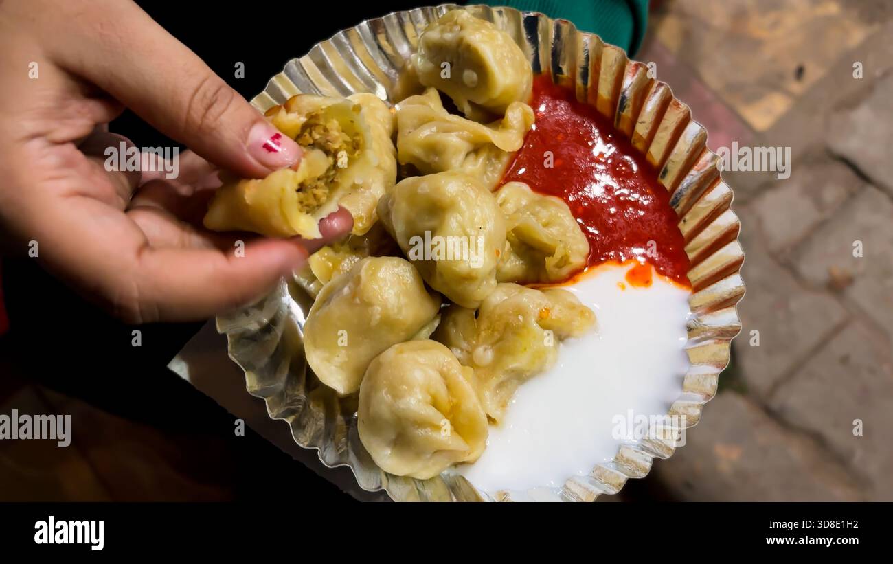 momos de rue cuits à la vapeur servis avec chutney rouge épicé et caillé sur une assiette jetable Banque D'Images