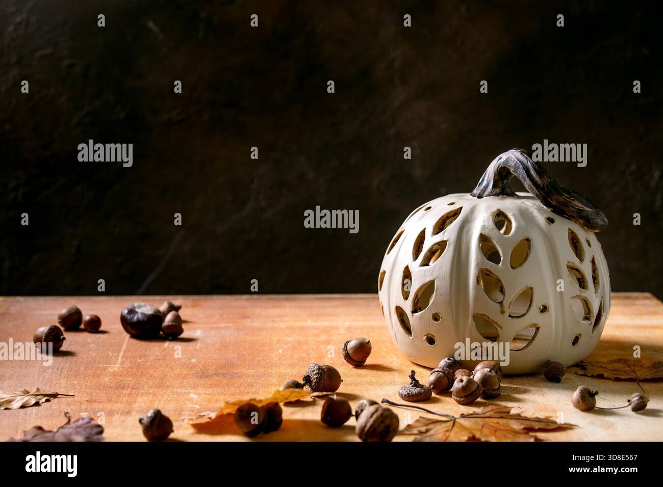 Décorations d'Halloween ou de Thanksgiving, citrouille en céramique sculptée blanche se tenant debout sur une table en pierre orange avec des feuilles d'automne et des glands. Décoration intérieure des fêtes d'Halloween. Copier l'espace Banque D'Images