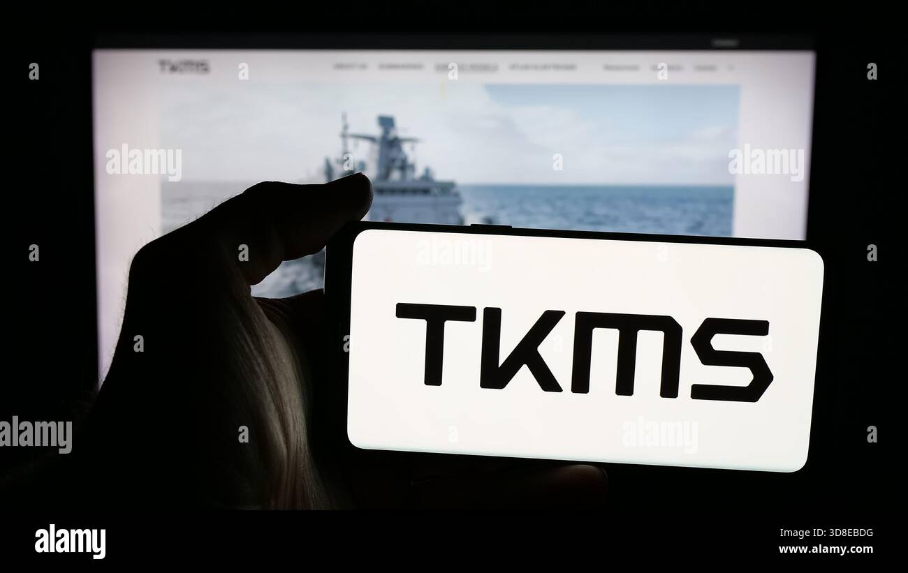 Stuttgart, Allemagne - 11-20-2025 : personne tenant un téléphone portable avec le logo de la société ThyssenKrupp Marine Systems (TKMS) sur l'écran devant la page web. Banque D'Images