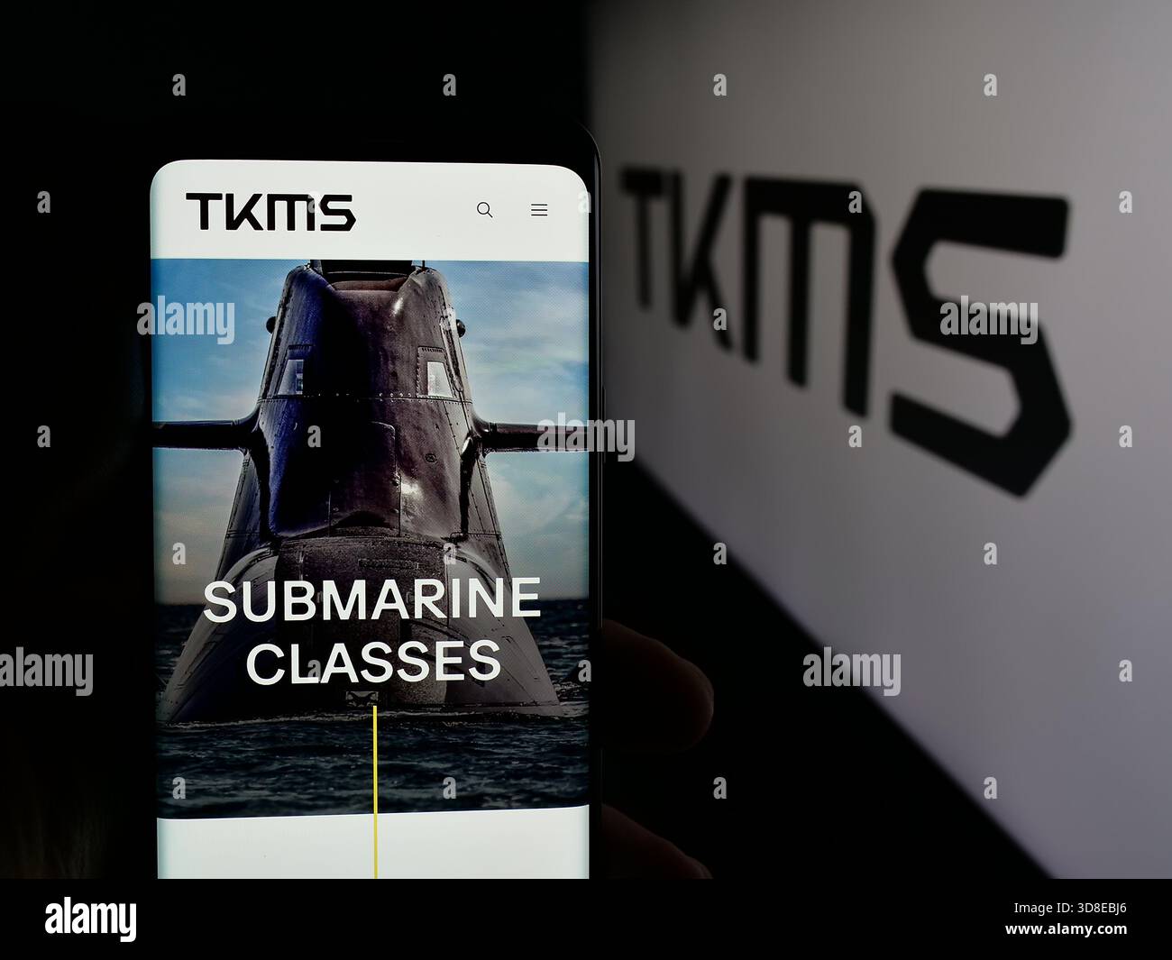 Stuttgart, Allemagne - 11-20-2025 : personne tenant un téléphone portable avec la page web de la société ThyssenKrupp Marine Systems (TKMS) sur l'écran devant le logo. Banque D'Images