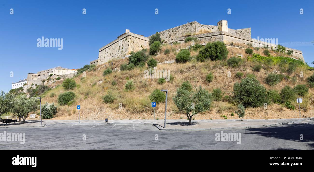 Large vue panoramique sur le château historique de Palmela au Portugal. La forteresse médiévale se trouve au sommet d'une colline haute, sèche et herbeuse au-dessus d'un parking moderne. Banque D'Images
