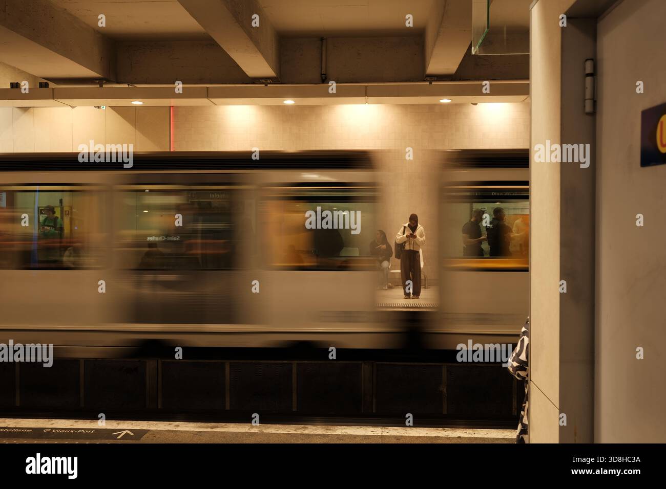 Train de métro flou passant par la gare de Marseille avec une jeune femme debout immobile sur le quai opposé, France. Banque D'Images