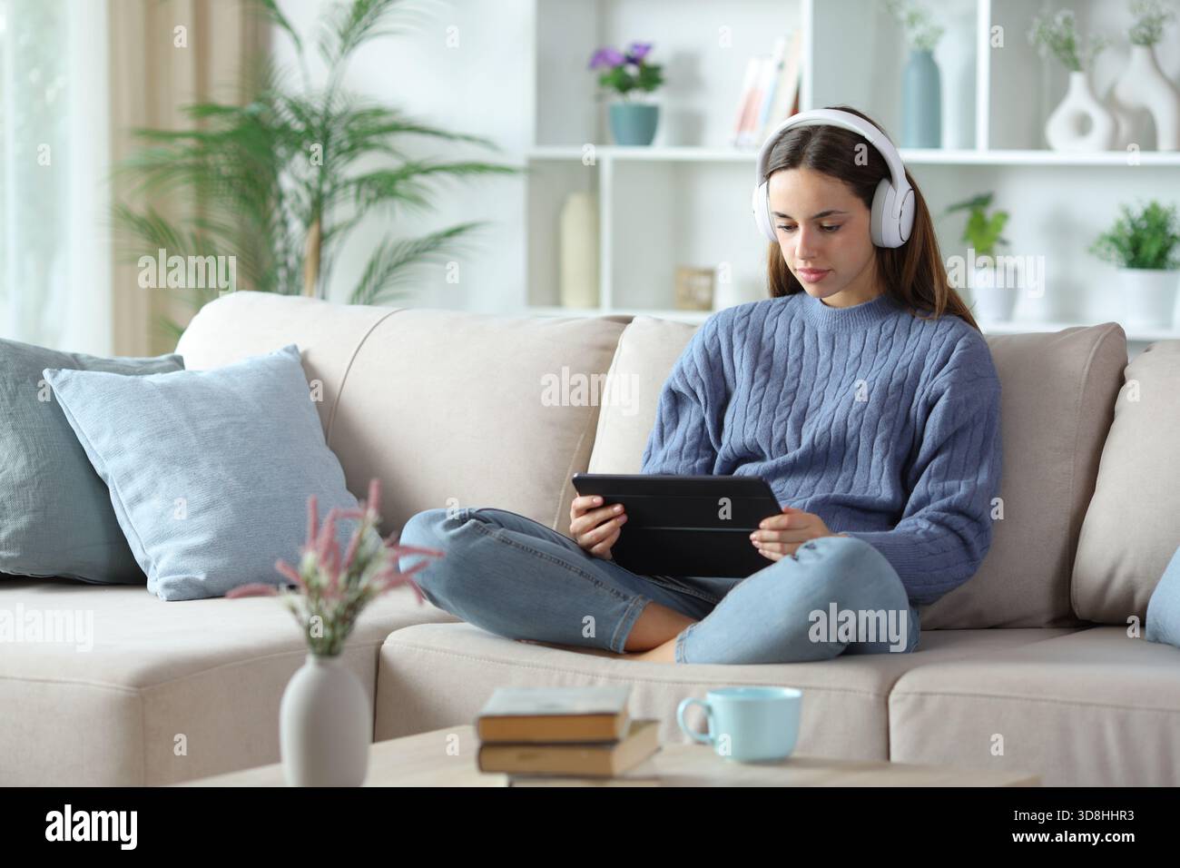 Femme en bleu portant un casque regardant le contenu en streaming sur tablette assis sur un canapé à la maison Banque D'Images