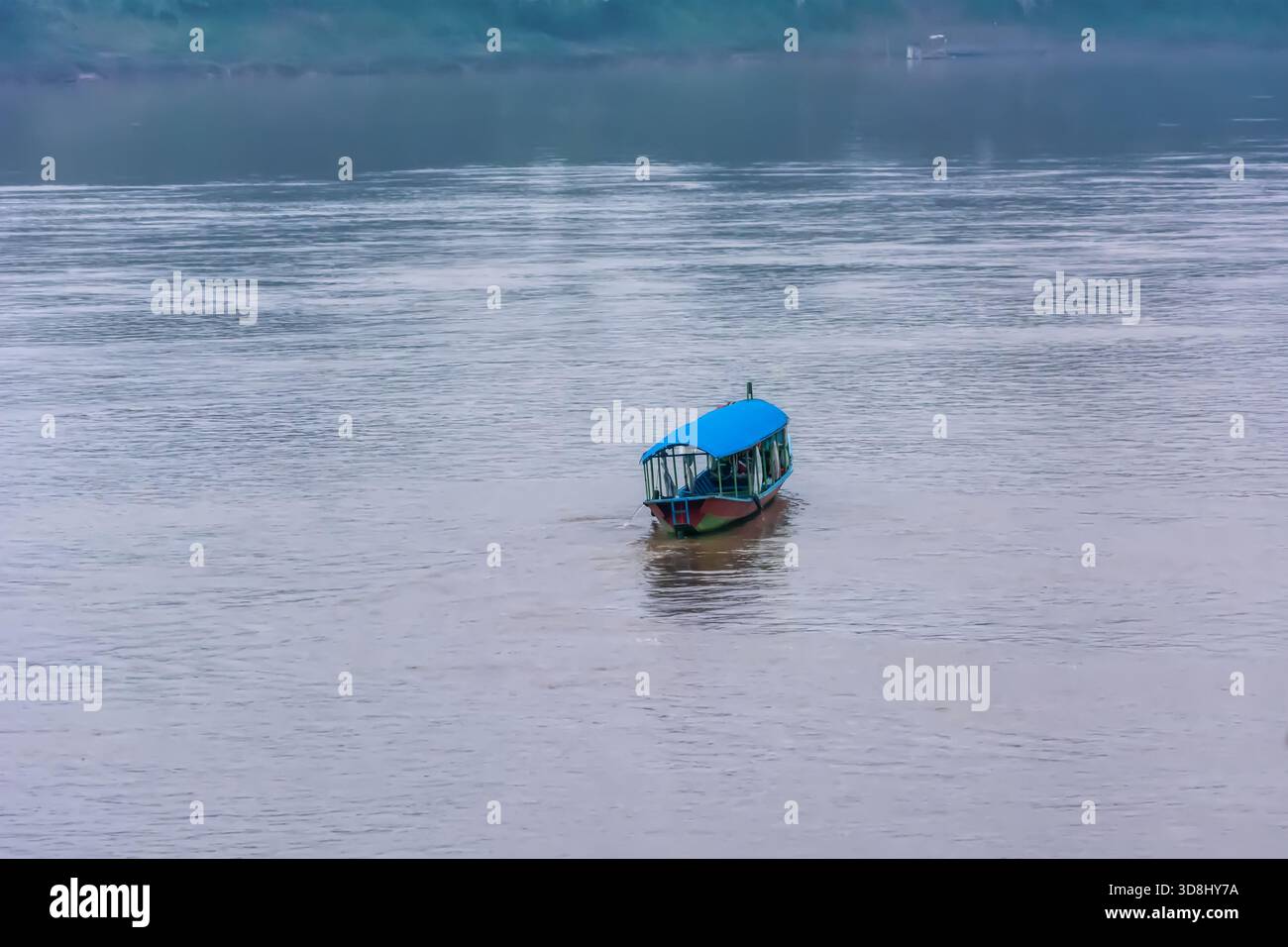 Bateau traditionnel à longue queue flottant doucement sur les eaux calmes du Mékong au cours d'une journée nuageuse tranquille, créant une atmosphère de voyage paisible. Banque D'Images